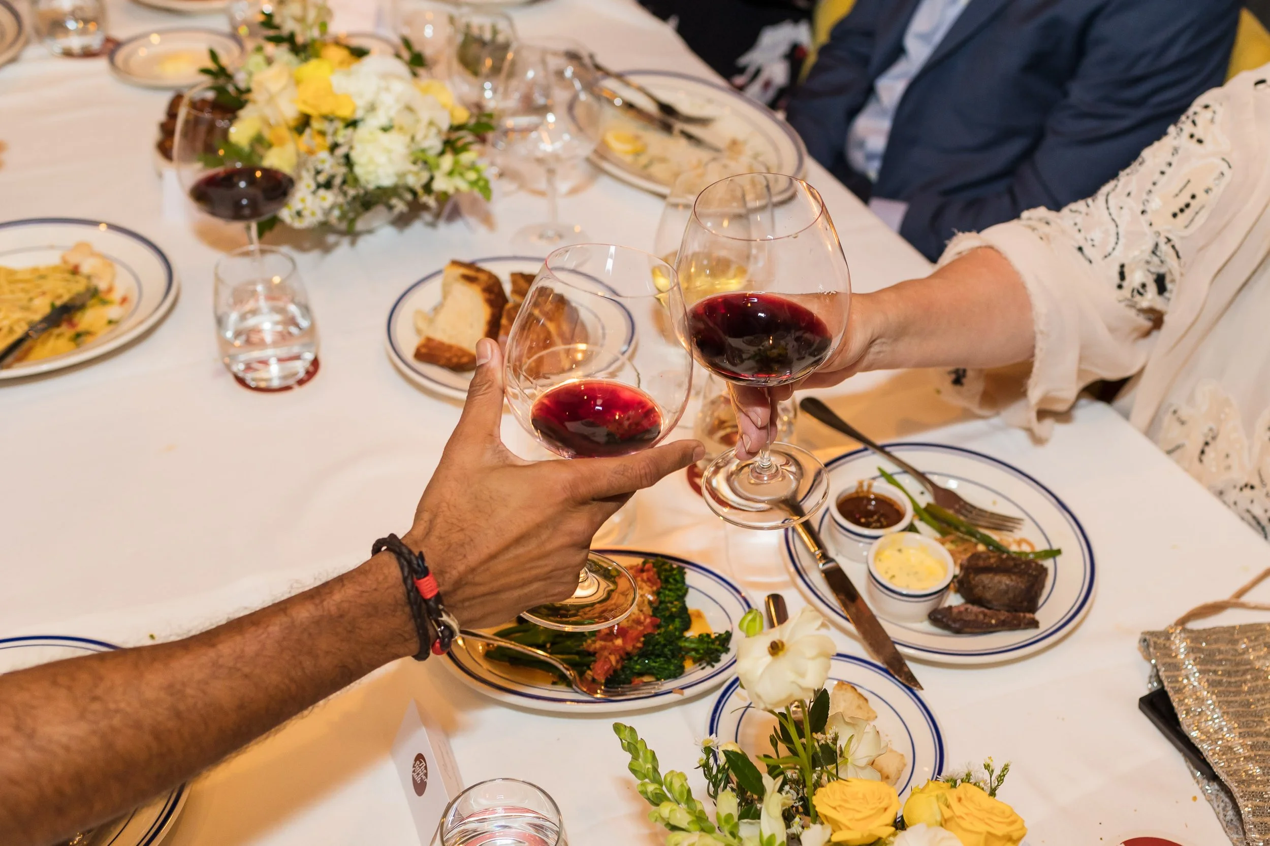 Guests at event clinking glasses of red wine over table