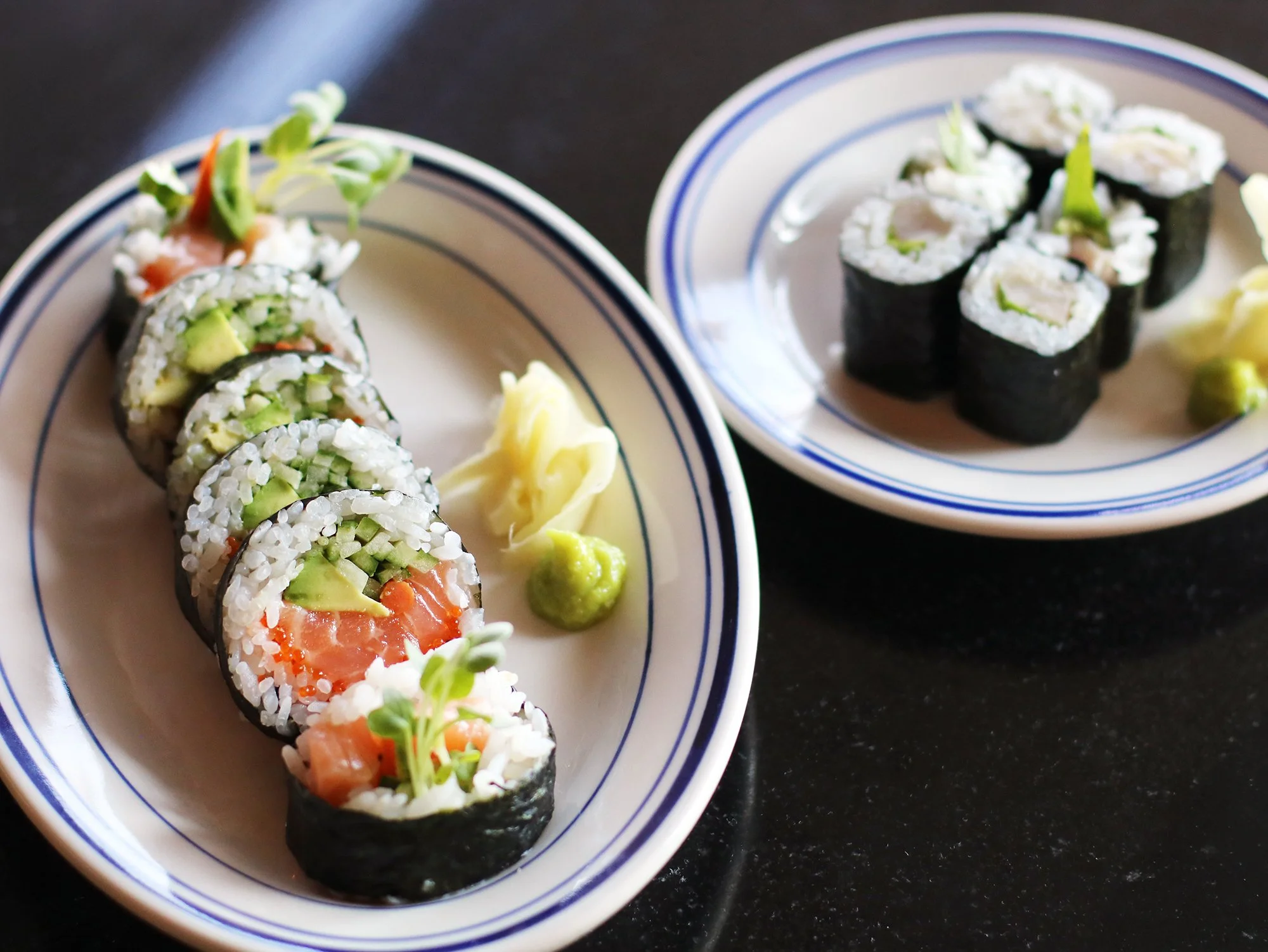 Two plates of sushi rolls- Salmon Maki on the left and Hamachi Hosomaki on the right.