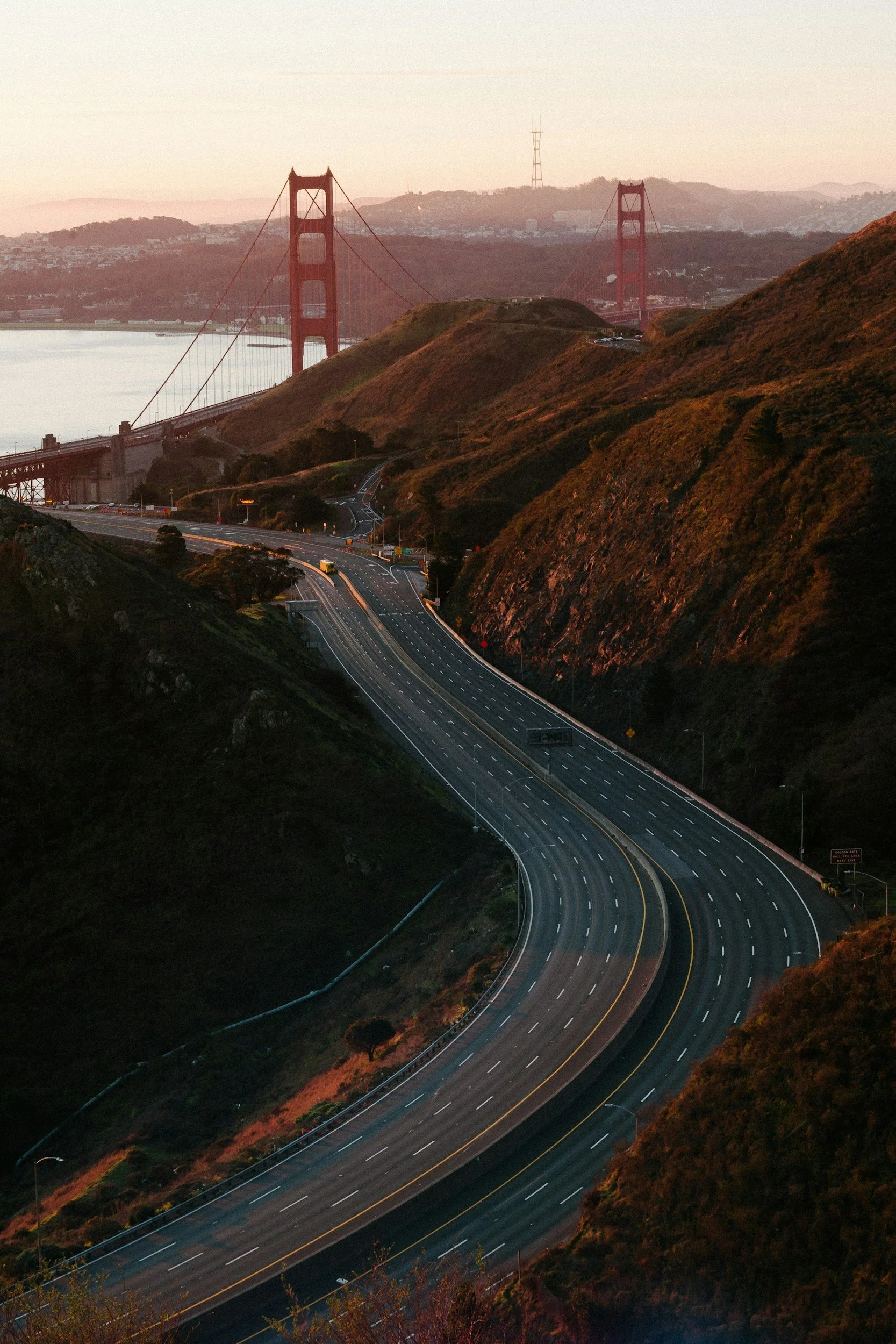 Golden Gate Bridge at sunset with empty highway winding through hills in San Francisco, California.