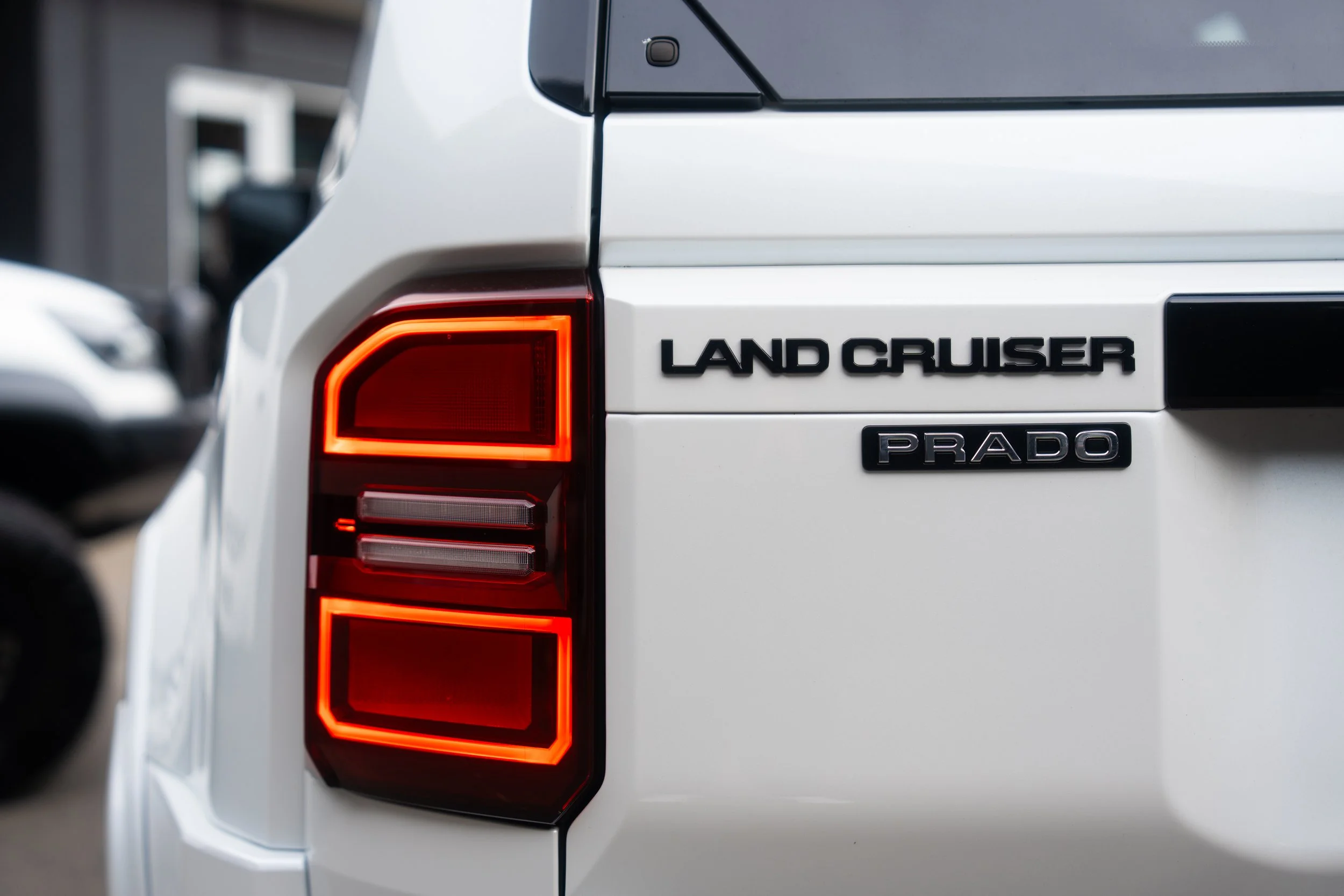 Close-up of the rear side of a white Land Cruiser Prado, showing the taillight and badges.