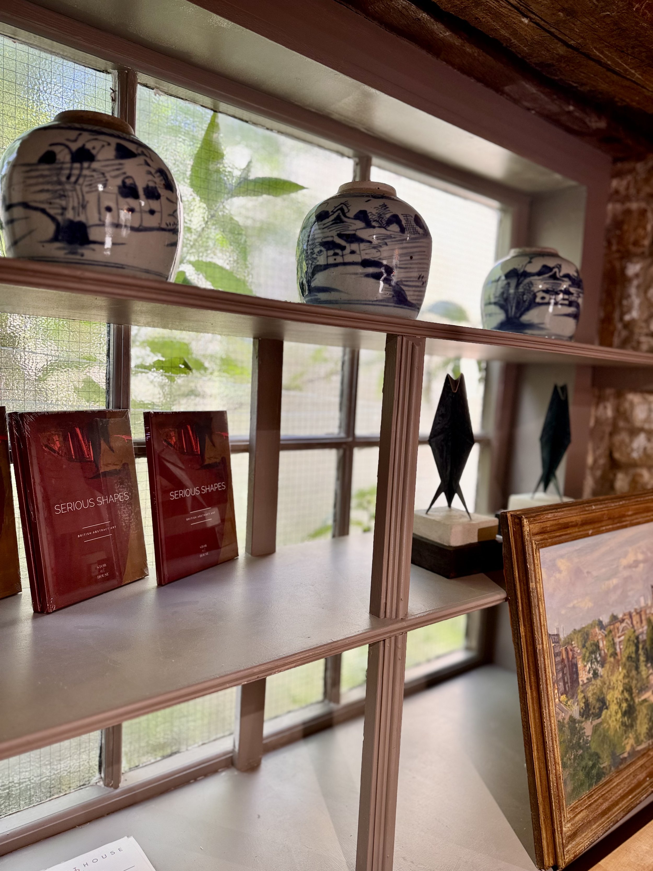 Shelf displaying three ceramic vases with landscape blue and white designs in front of a window with green leaves outside.