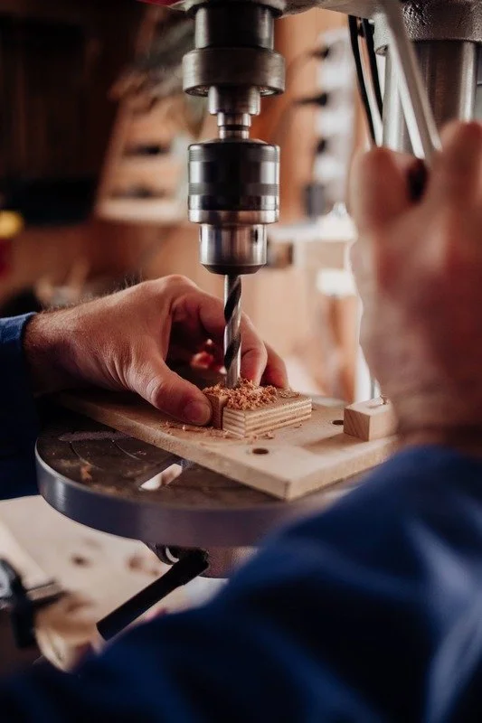 Une personne utilise une perceuse pour faire un trou dans un morceau de bois à l'aide d'une machine électrique dans un atelier de menuiserie.