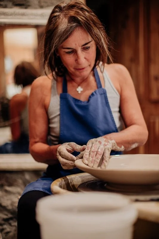 Femme en tablier bleu façonnant de la poterie sur un tour en argile dans un atelier