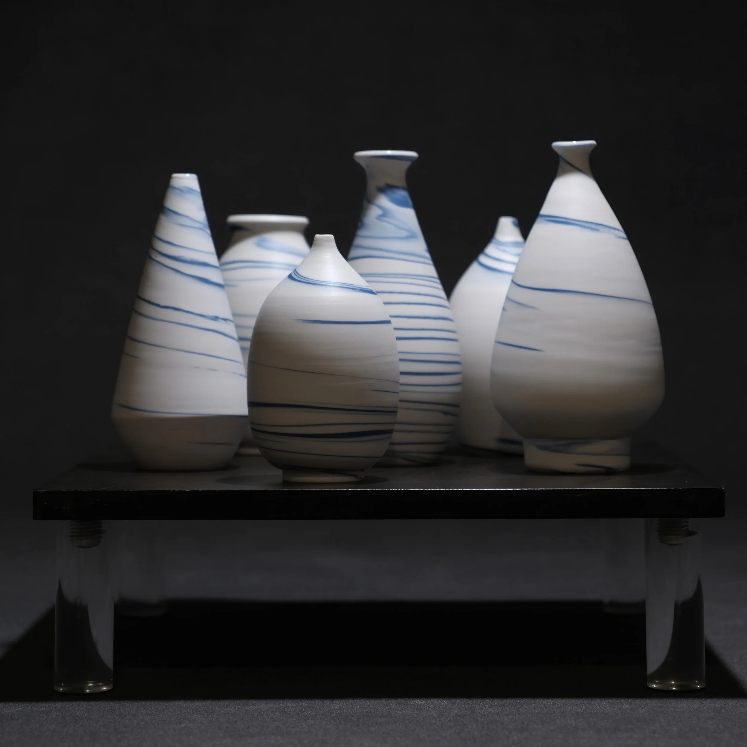 S W I R L - the focus is on action and movement. Blue and white porcelain wheel thrown vessels that aim to create swirls and twirls of movement.  Visually spinning even though stationary.  Clear glazed interiors with diamond-polished naked exteriors 