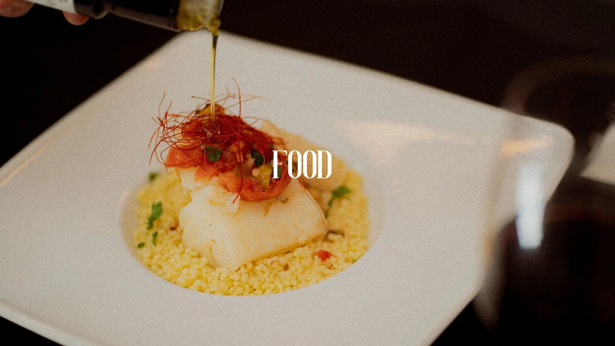 A plated gourmet dish with a scoop of white sorbet on yellow couscous, topped with thin strands of red garnish, and a drizzle of oil, served on a white square plate.