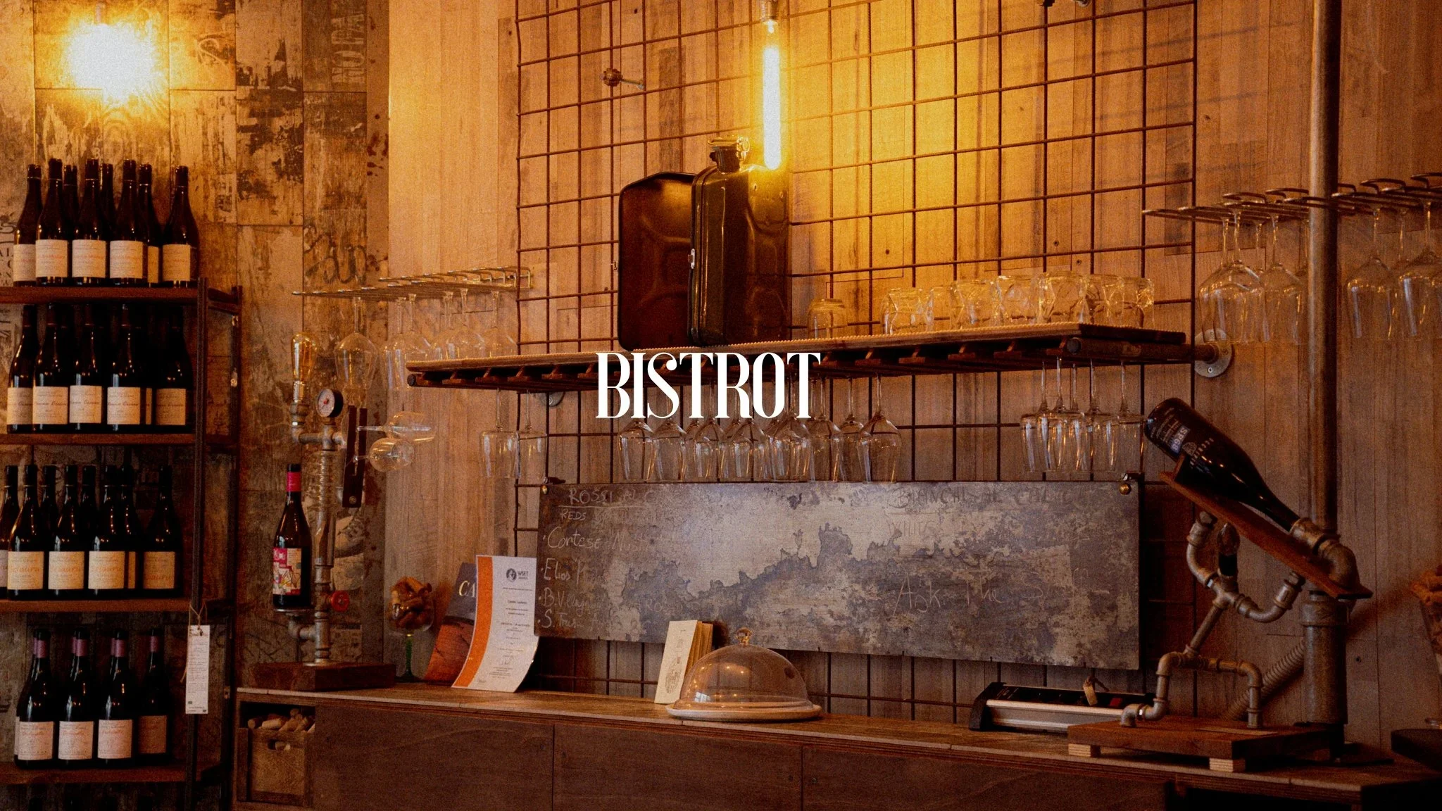 Interior of a rustic bistro with shelves of wine bottles, hanging glasses, lifting equipment, and warm lighting.