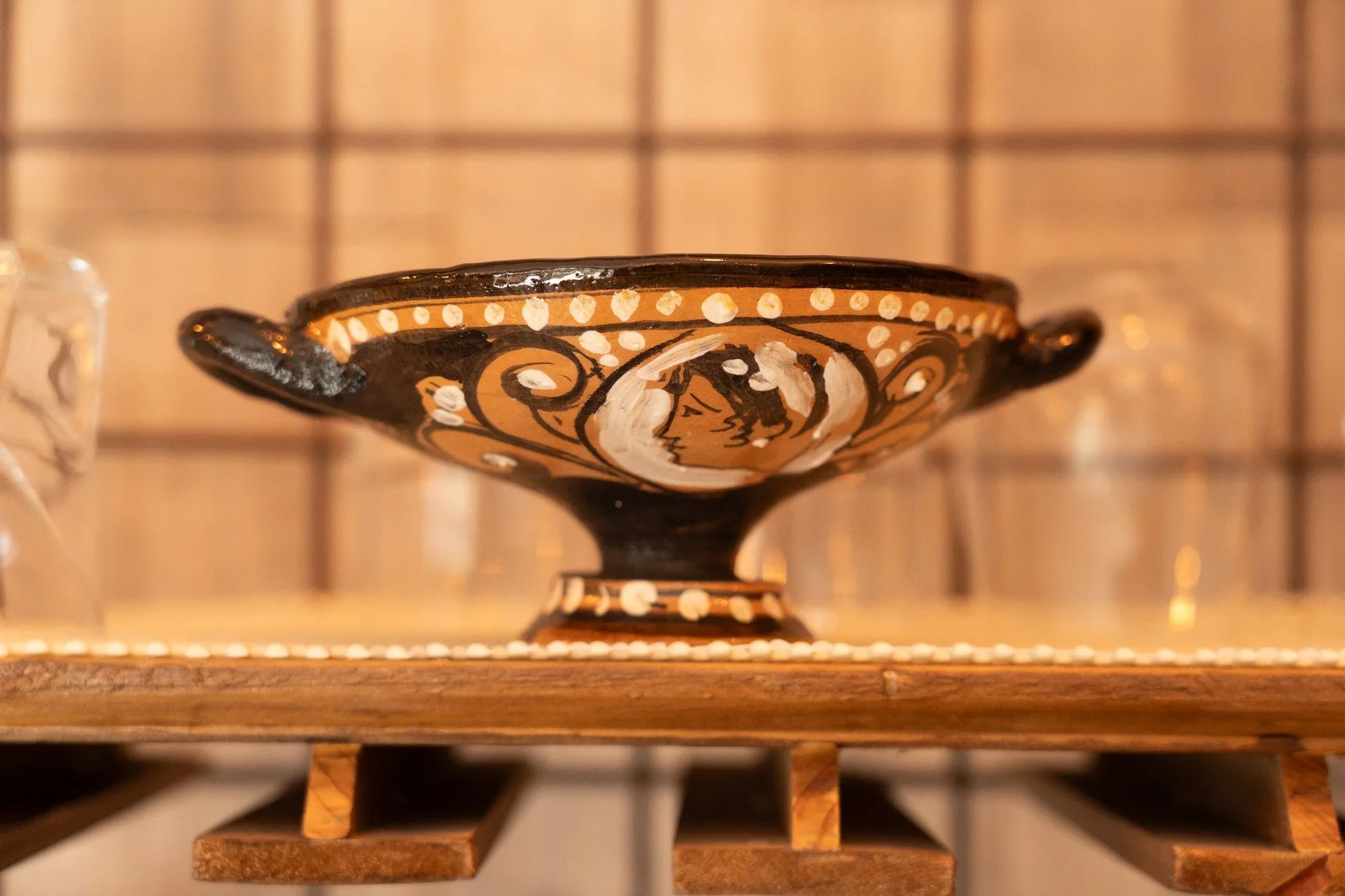Ceramic bowl with black and beige decorative designs, featuring a woman's profile surrounded by swirls, on a wooden shelf.