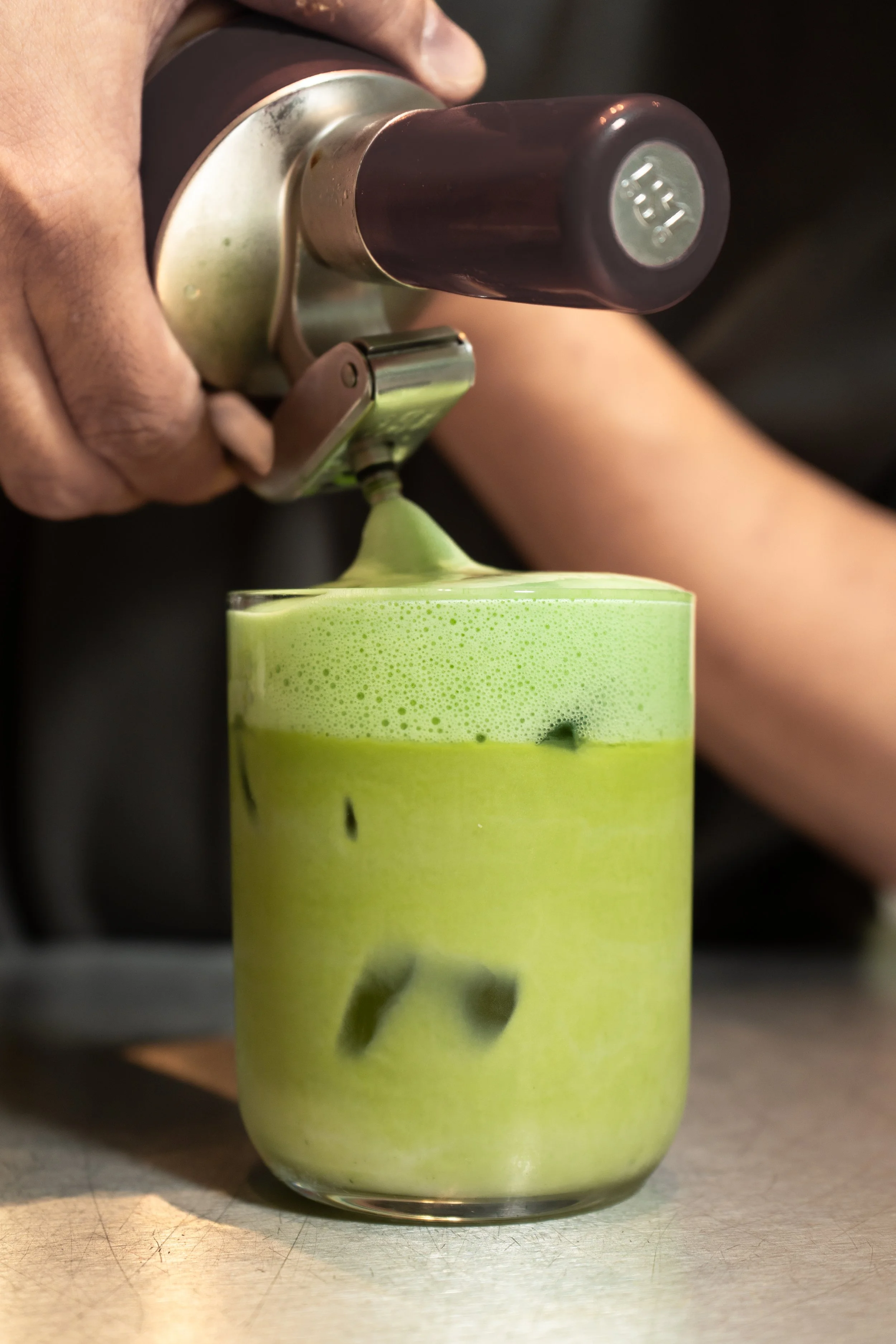 A person pouring pandan foam on top of a matcha latte