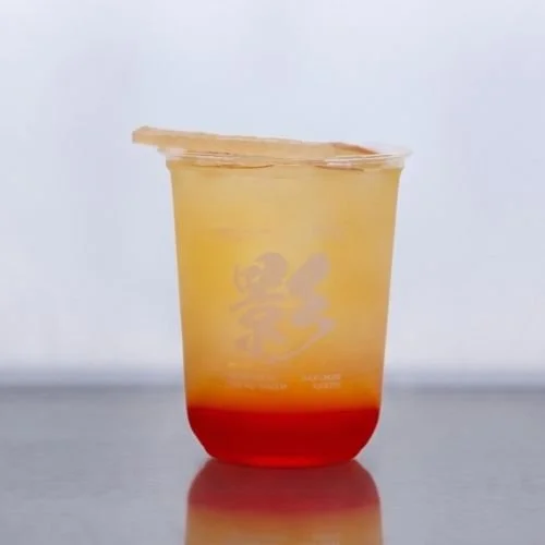 Layered beverage with a red bottom, orange middle, and yellow top in a clear plastic cup, topped with a crystal candy