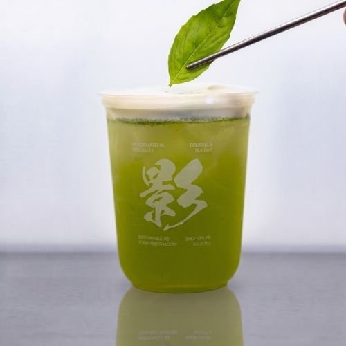 A cup of mixed tea and basil with a fresh basil leaf held by chopsticks above it.