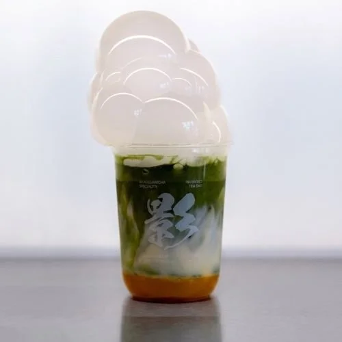 A layered matcha latte with mango and passionfruit in a clear cup topped with bubbles.