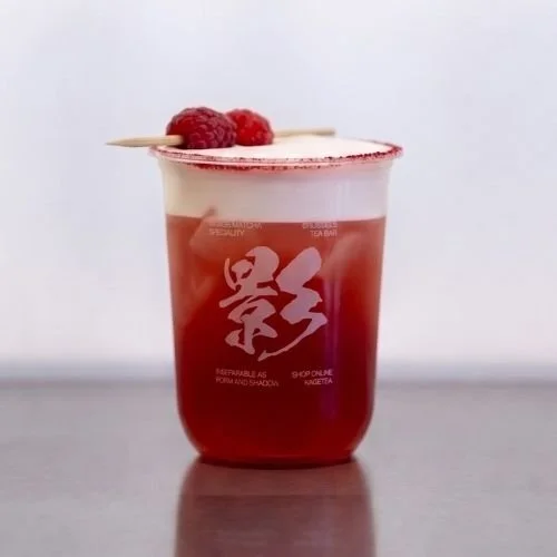 A red berry cocktail with a foam top, garnished with raspberries and a thin wooden skewer, in a clear cup.
