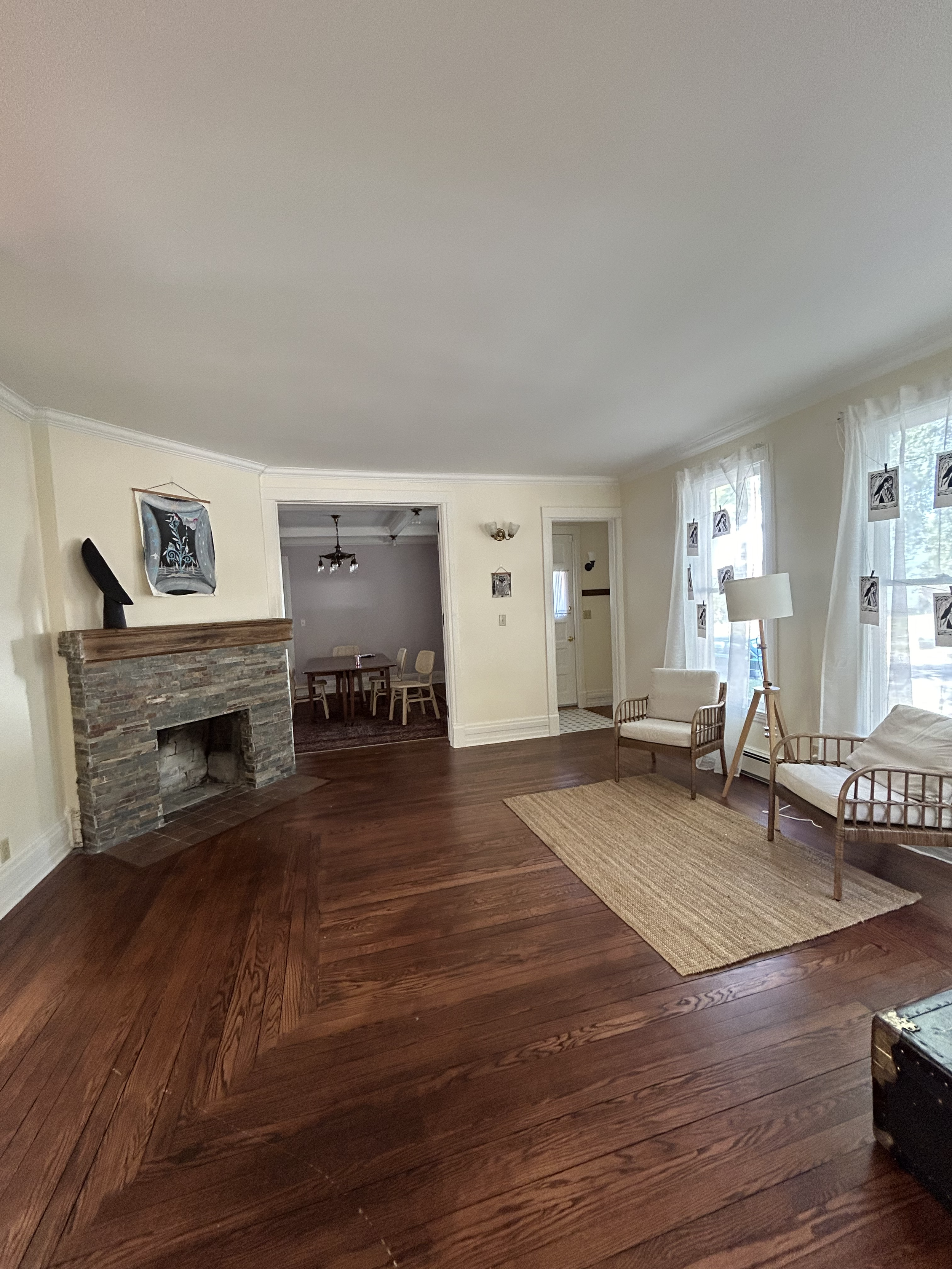 Living room with hardwood floor, stone fireplace, wicker chairs, and a rug; dining room visible through doorway.