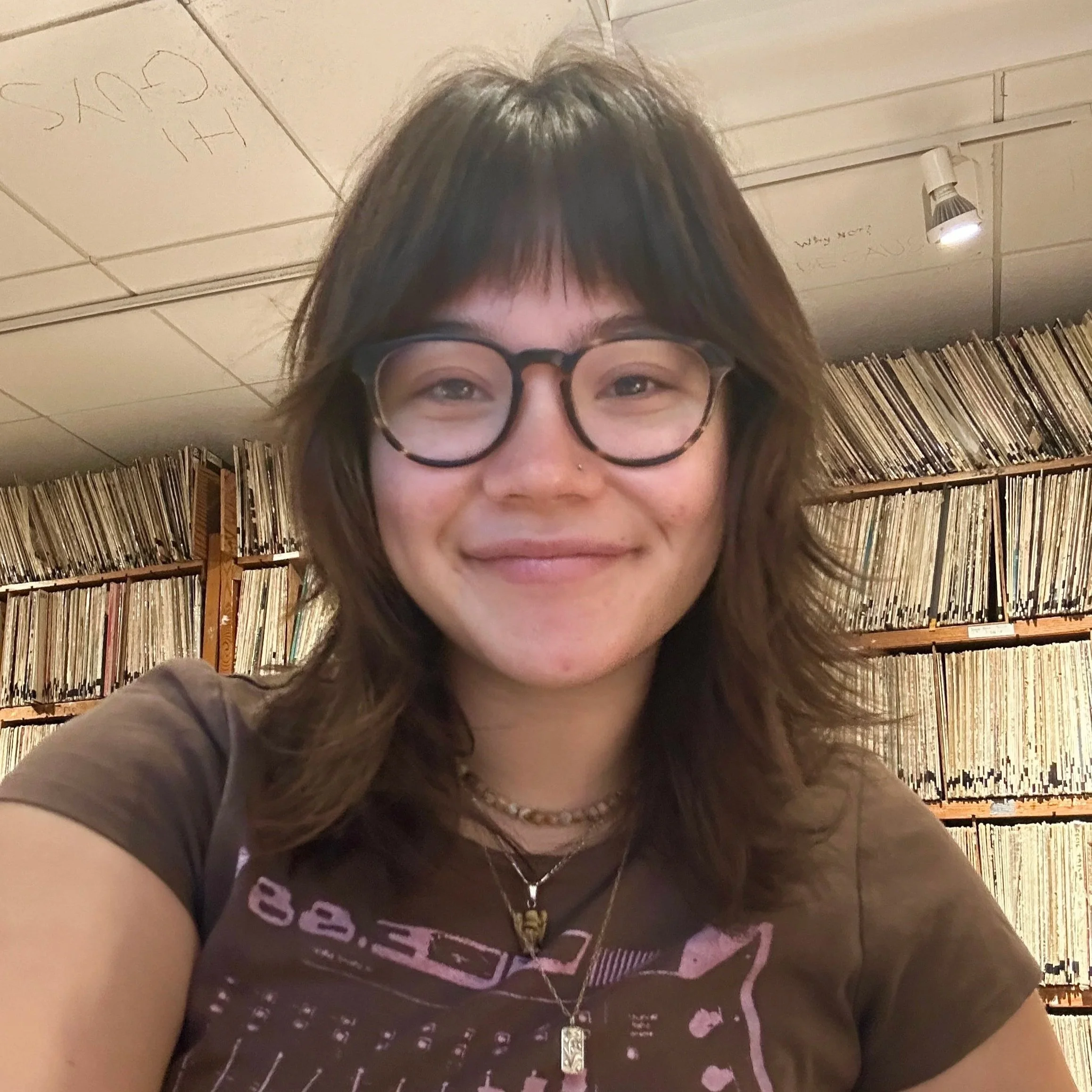 Mia is smiling with a wall of vinyl records in the background.