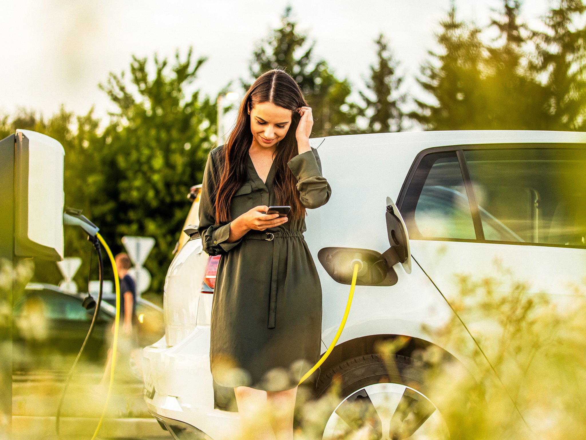Vrouw maakt zich klaar om een elektrische auto op te laden in een parkachtige omgeving.