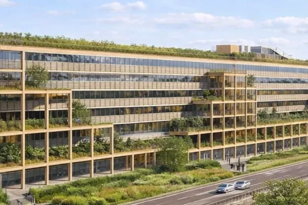 Modern kantoorgebouw met veel raam en groene balkons, gelegen langs een weg met auto's.