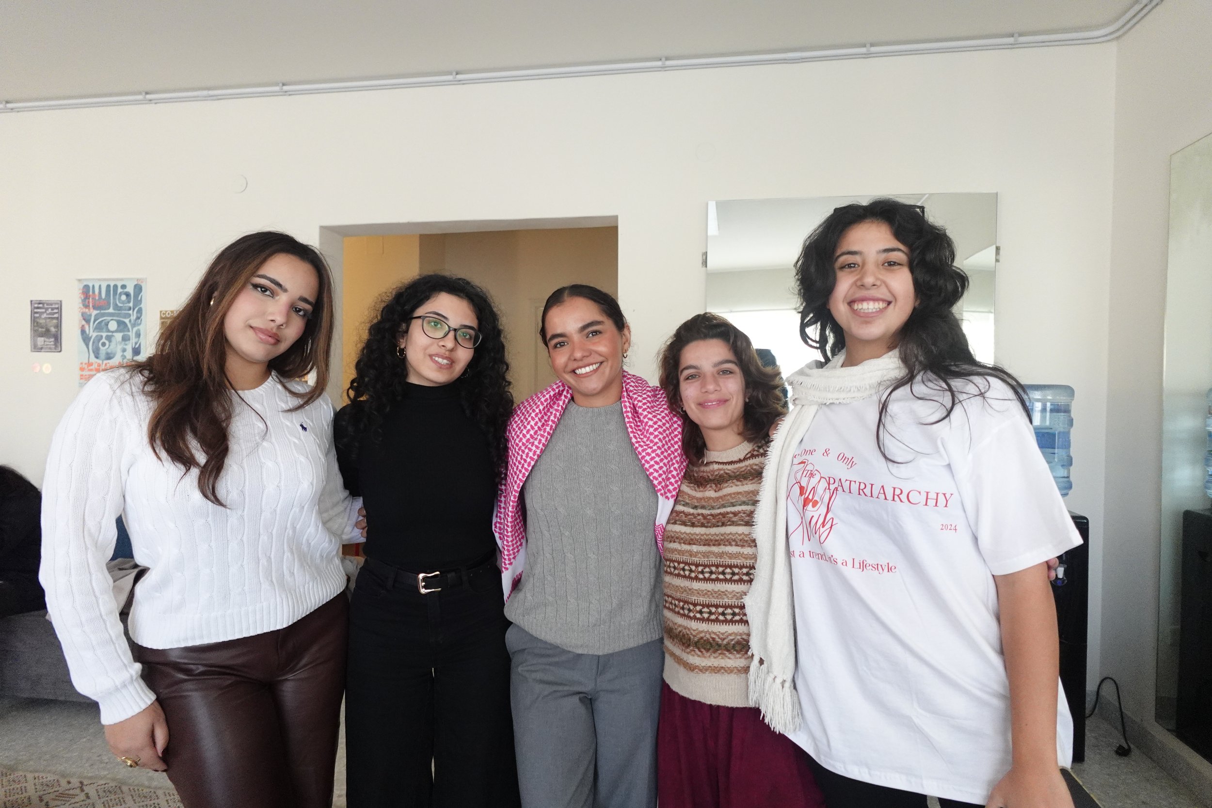 Five women standing together indoors, smiling at the camera.