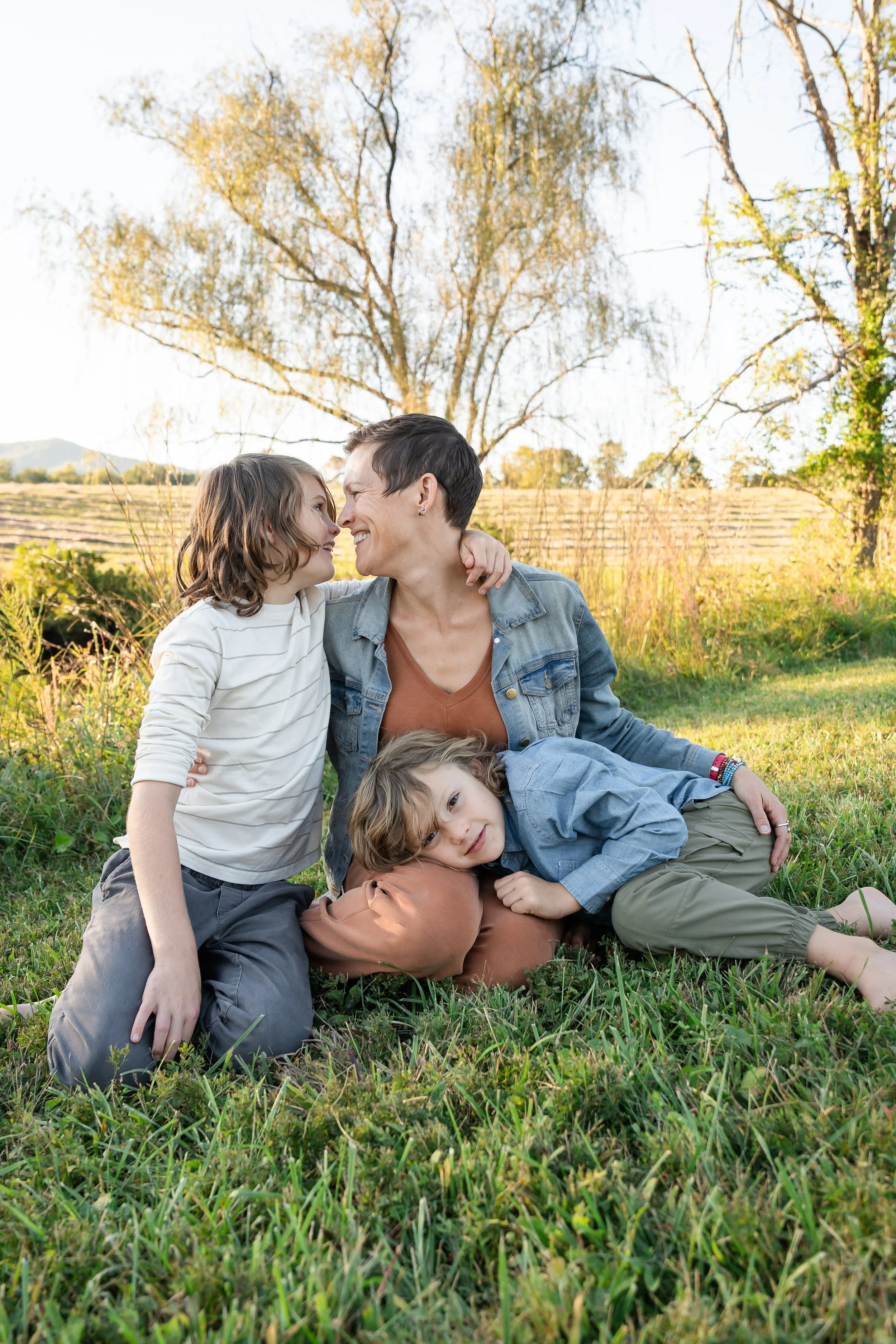  Mother and her two boys sitting close together beneath the trees during their autumn family portrait session at Grey Oaks Farm. 