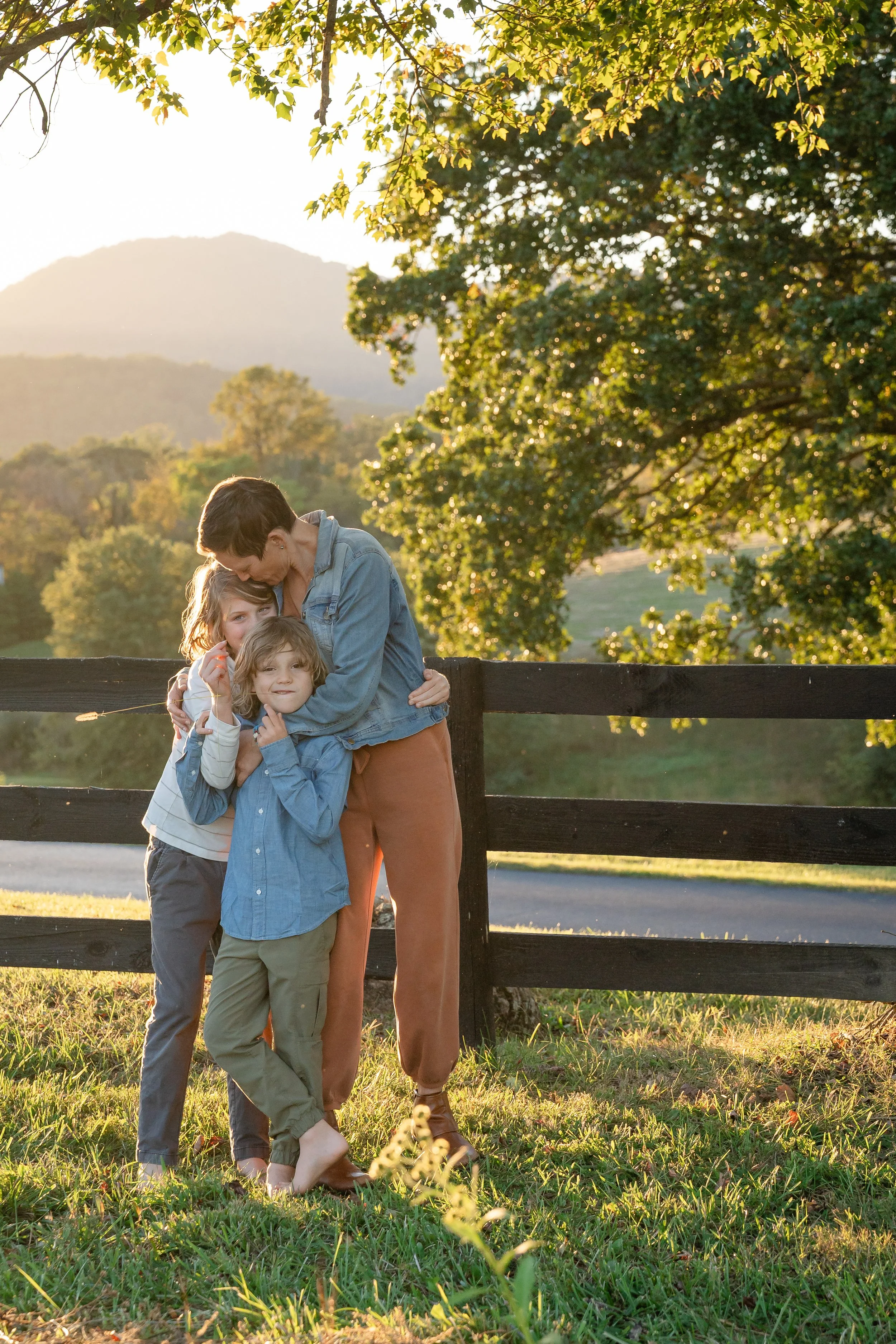  Mother embracing her two sons in golden evening light with autumn trees and the Virginia mountains behind them. 
