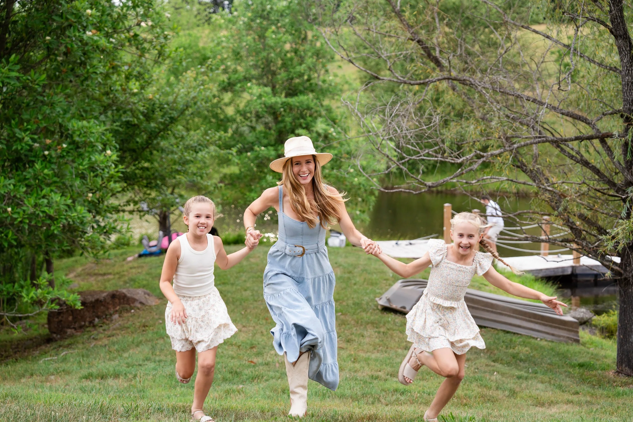  Mother in a blue dress running hand in hand with her two daughters beside the pond at Grey Oaks Farm, Charlottesville, VA 