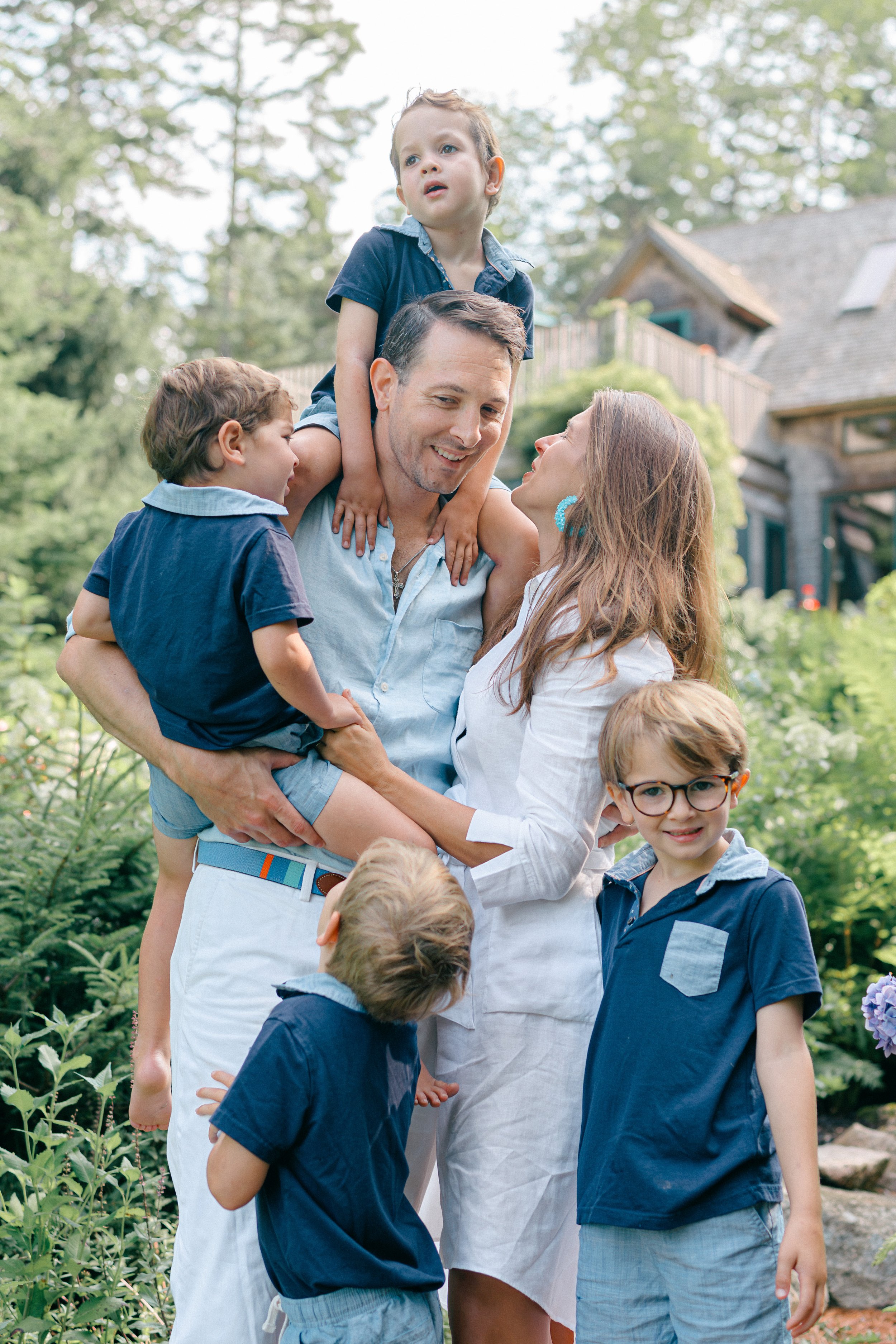 Father carrying his young son on his shoulders while mother laughs beside them during a Maine family photography session