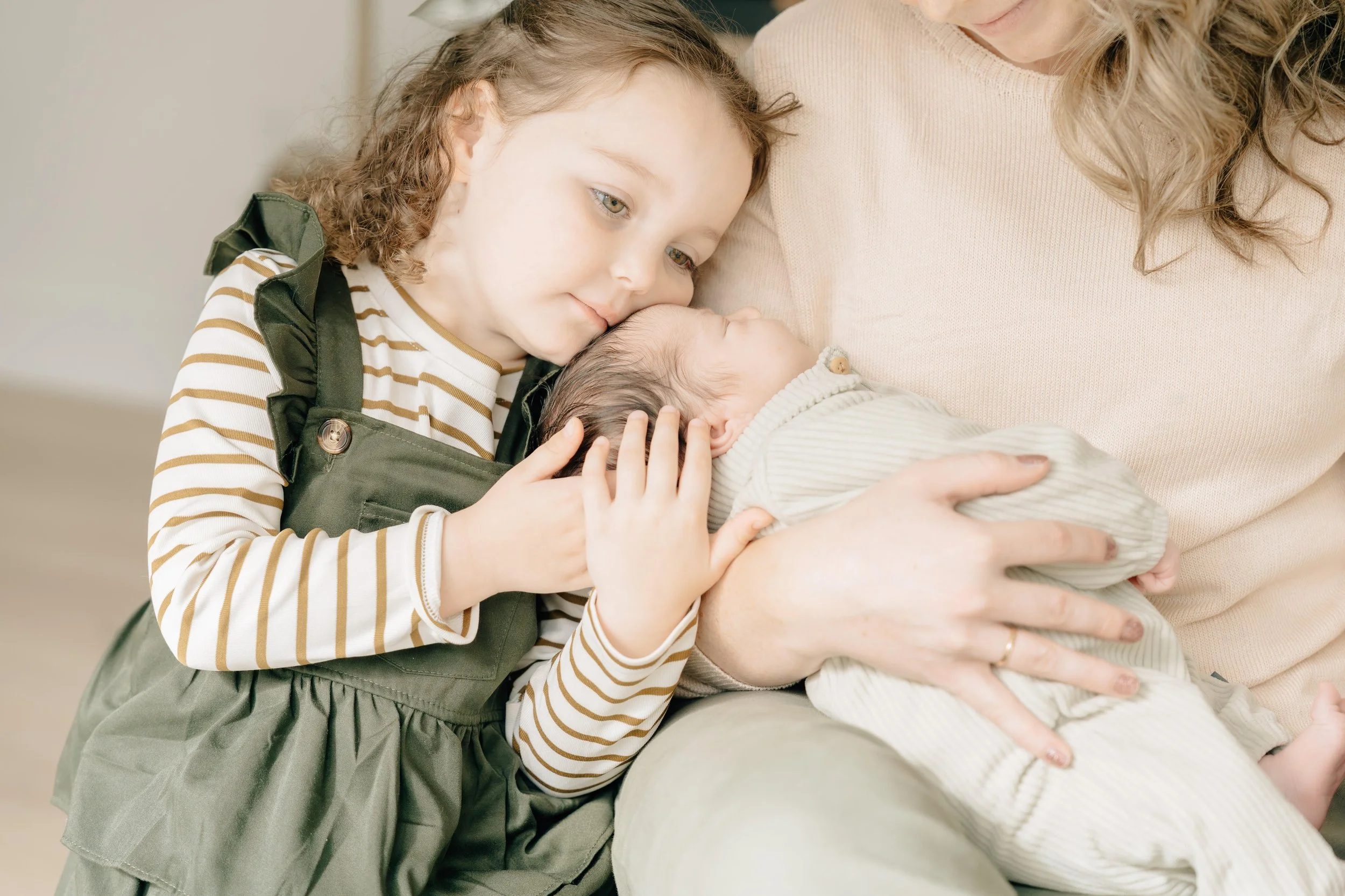 Young girl kissing a newborn baby held by their mother during a newborn photography session