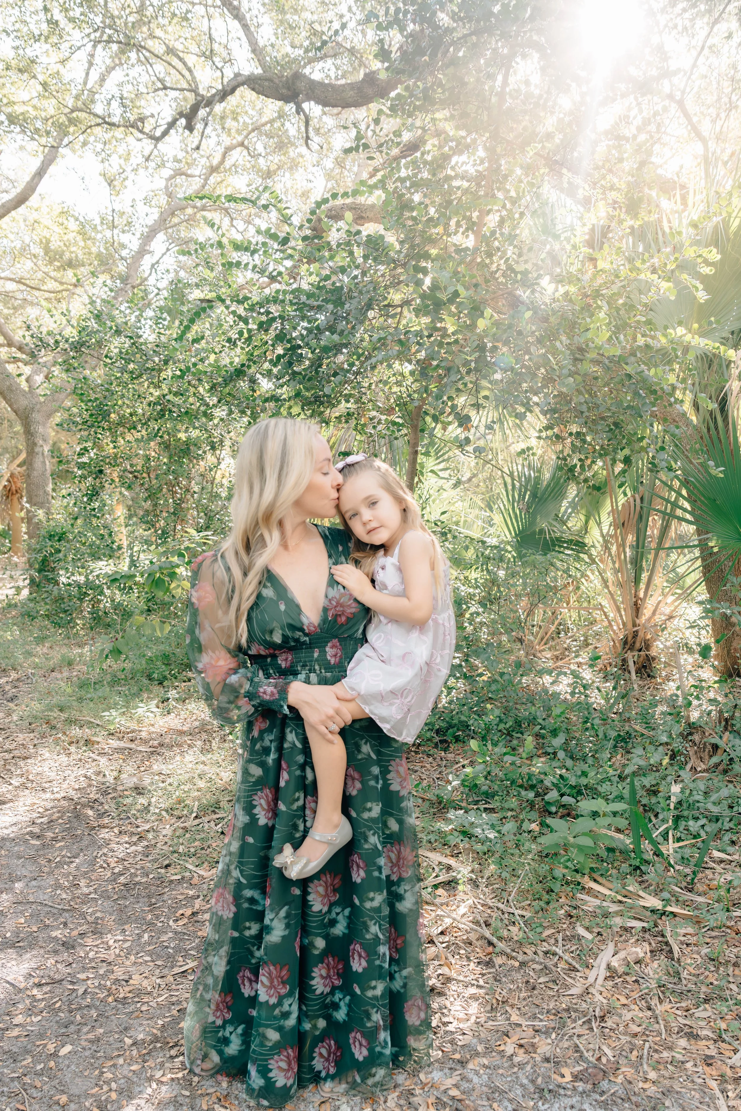 Mother and child sharing a tender moment outdoors, with warm sunlight illuminating the mother's face during a natural light family photography session.