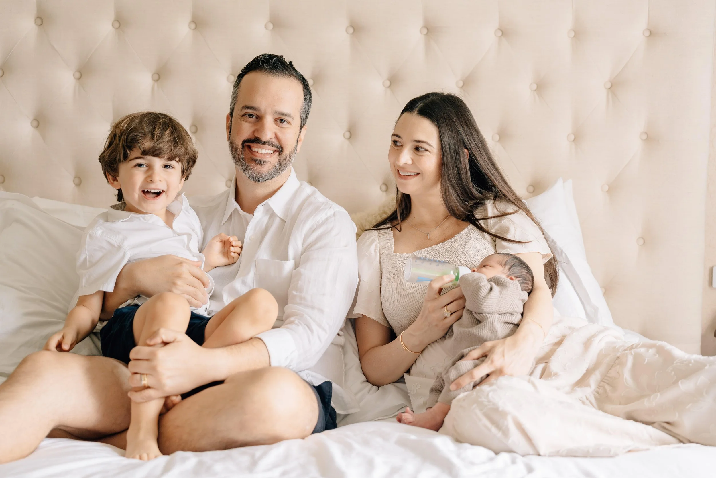 Family cuddled together on a tufted beige bed.