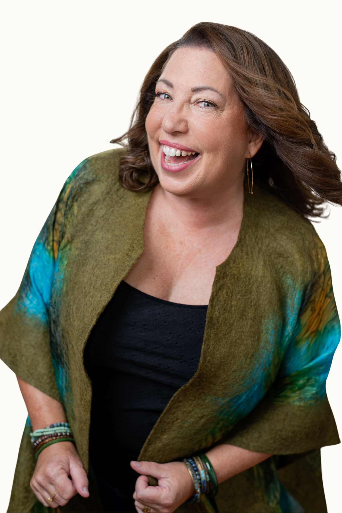 Sara Bird Nelson, energy guide,  smiling and laughing, wearing a black top and a colorful wrap with green, blue, and yellow hues, accessorized with bracelets and earrings.