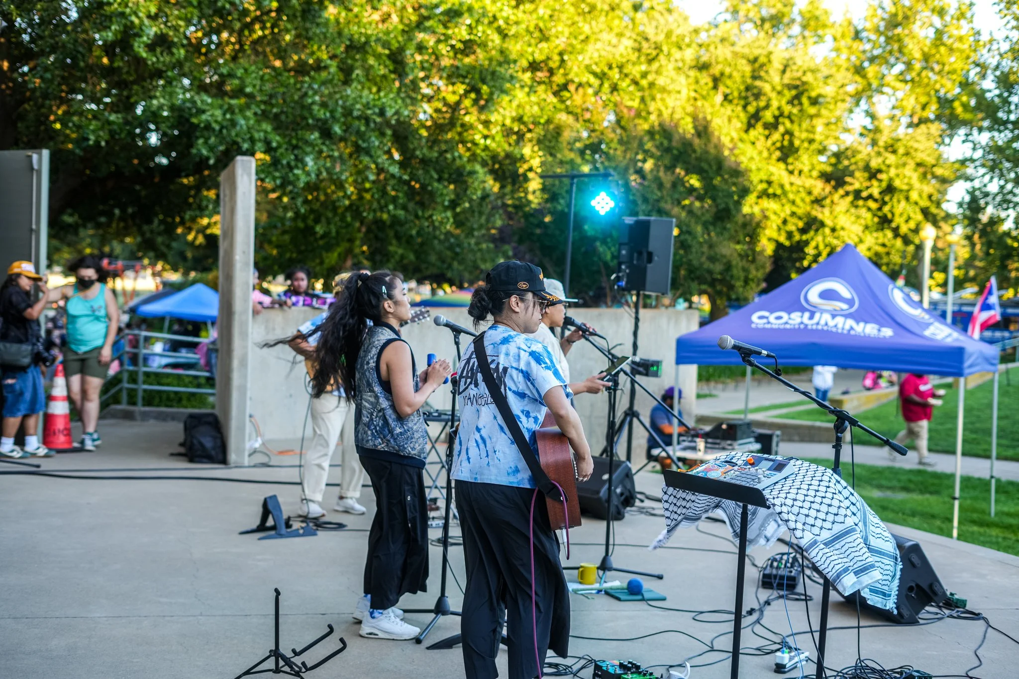 Side-stage view of a live band performing with professional live sound rental, PA speakers, microphones, and audio engineering at an outdoor Sacramento event.