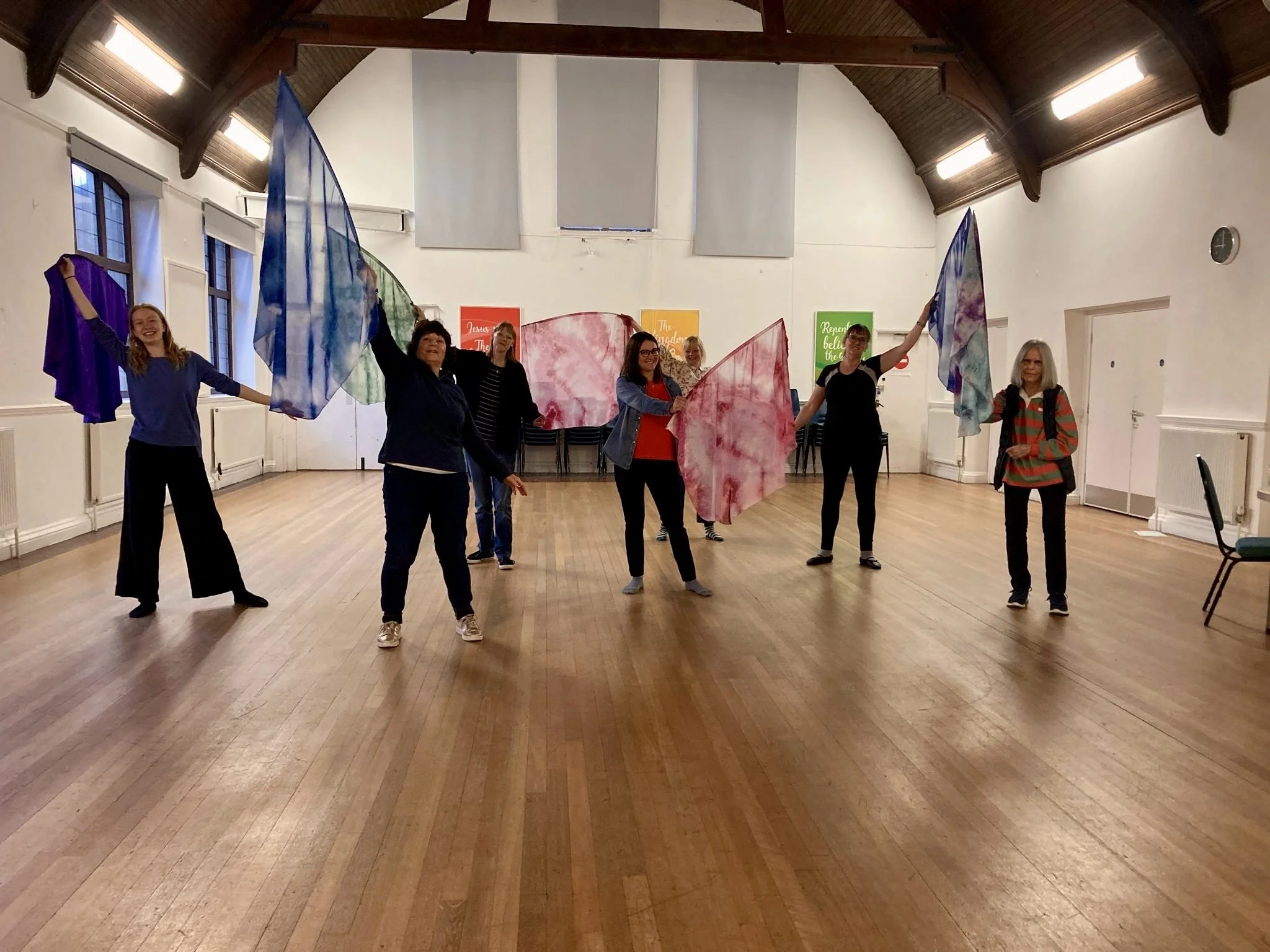 A group of women stand in the middle of a hall lifting up colourful flags