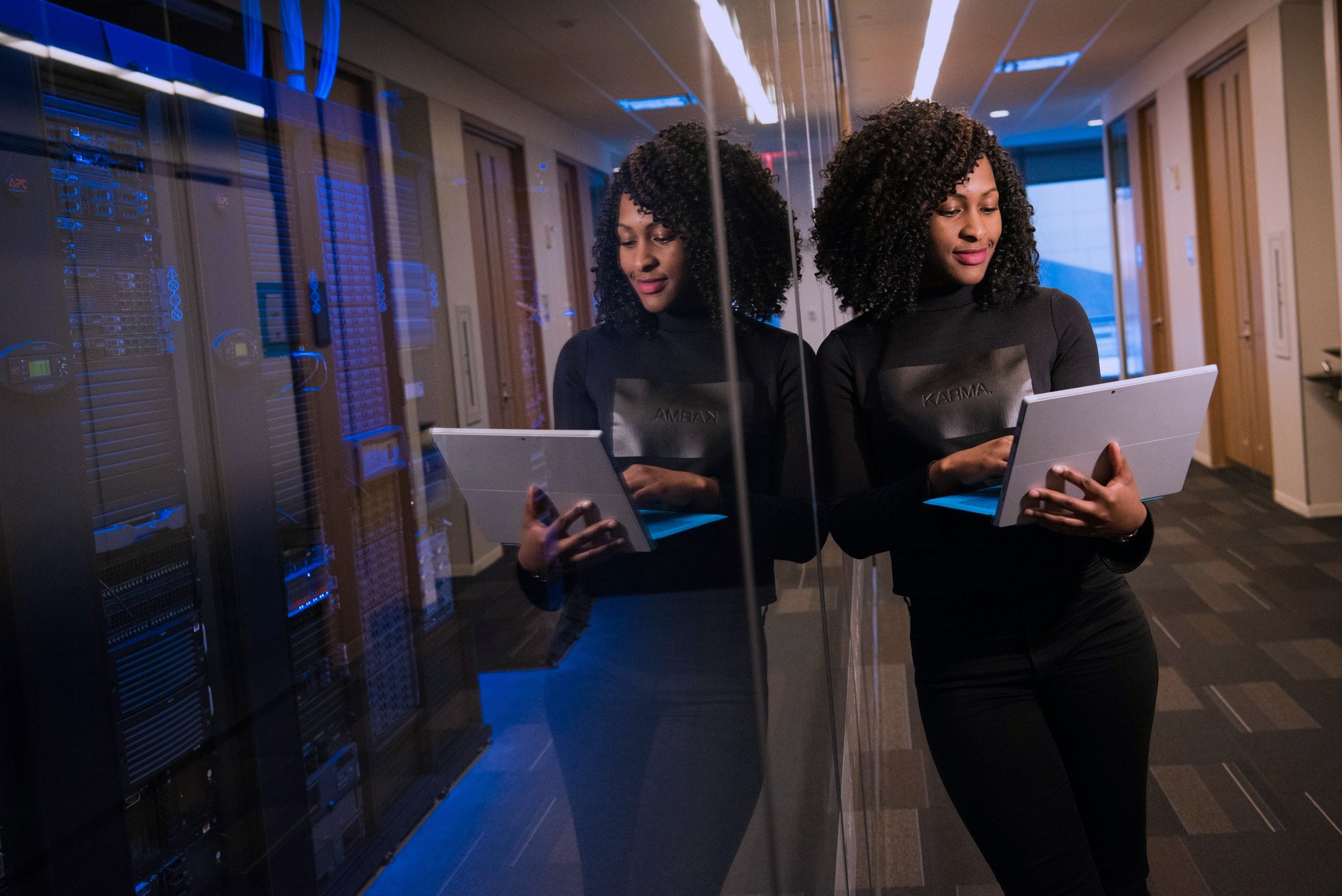 Woman on laptop leaning up against glass housing technology hardware