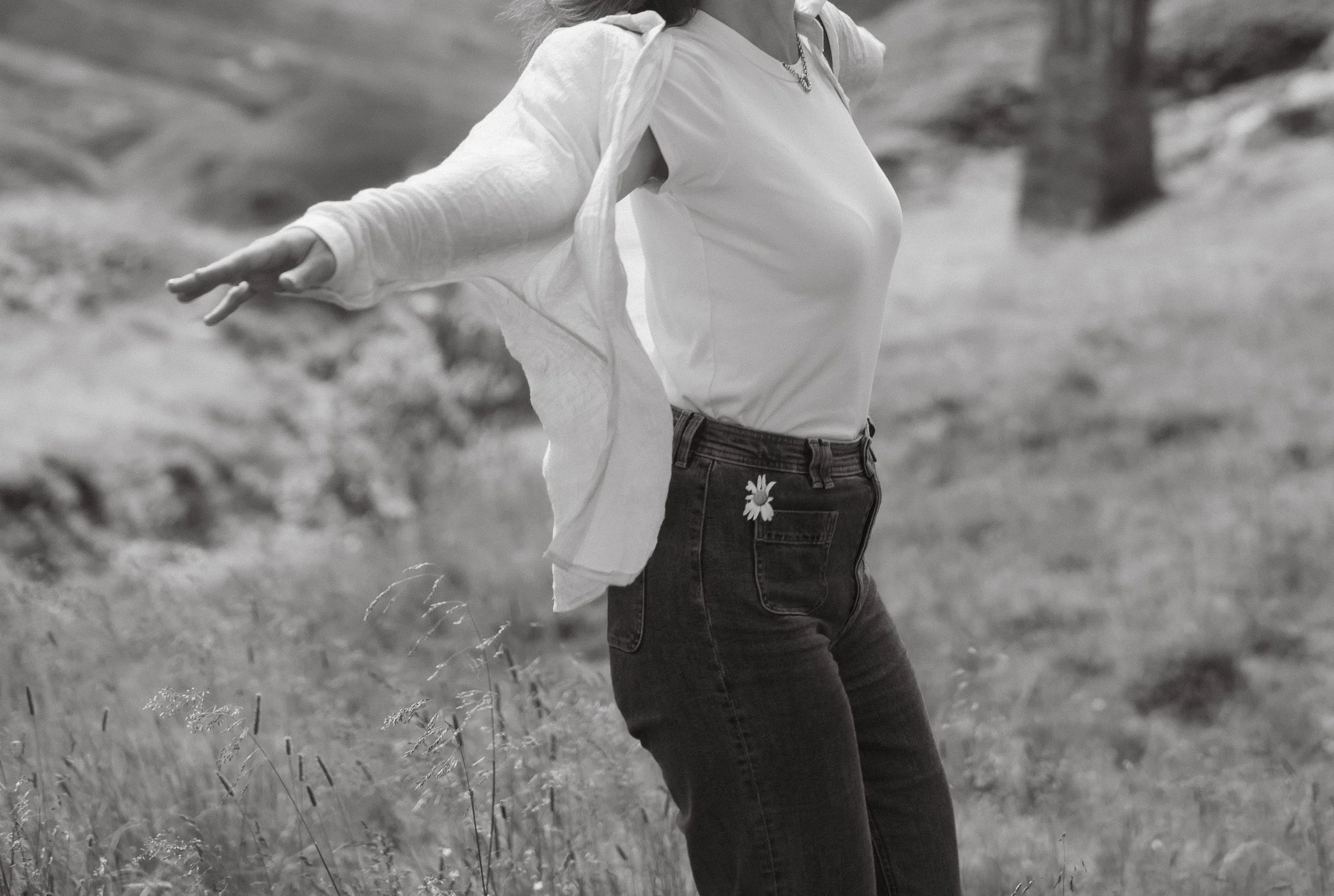 Schwarze und weiße Aufnahme einer Person, die im Freien tanzt, mit offenem Arm und hinter sich eine Wiese mit Bäumen.