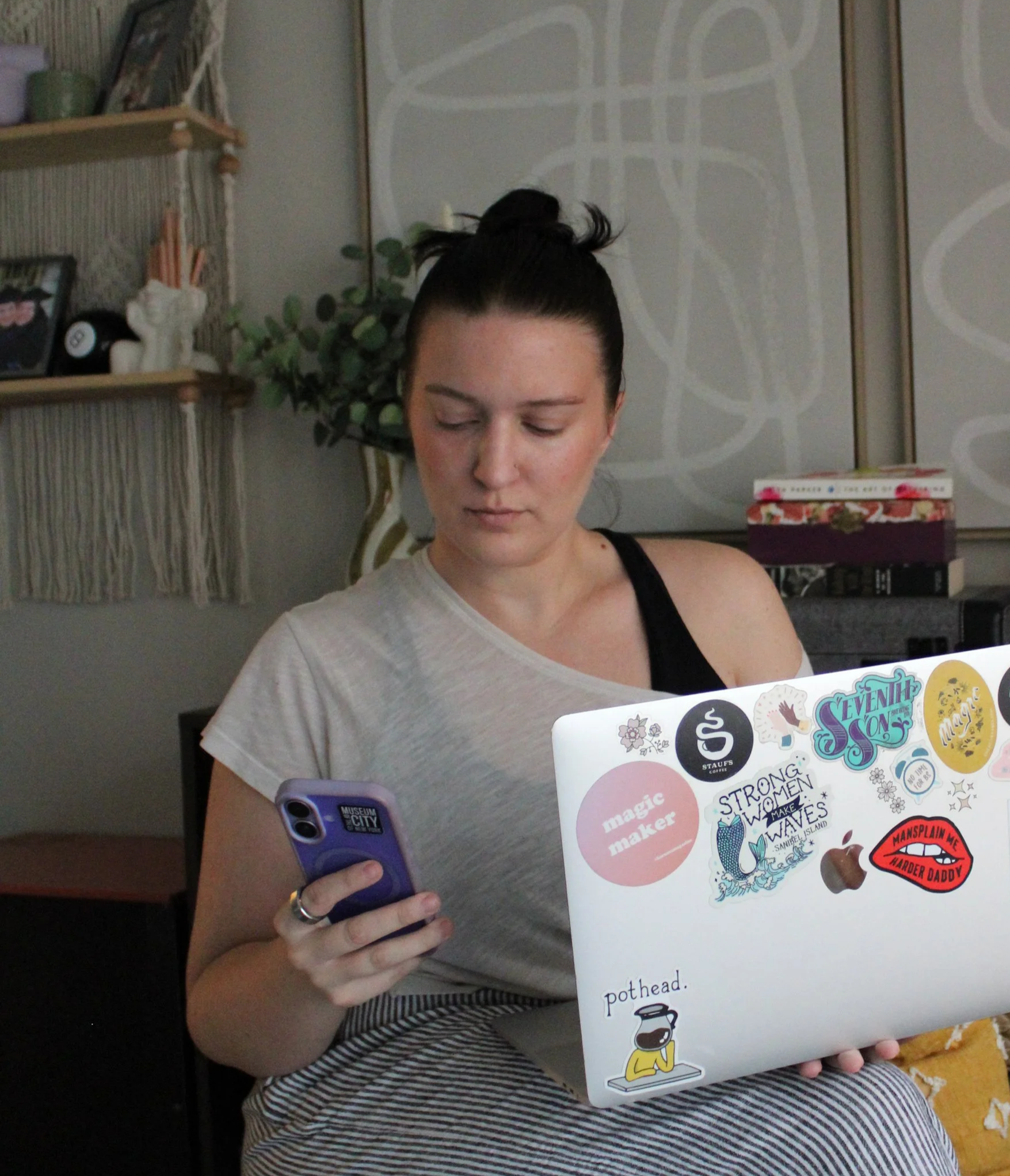 Diana looking at her phone in one hand, and holding her laptop with colorful stickers on it in the other