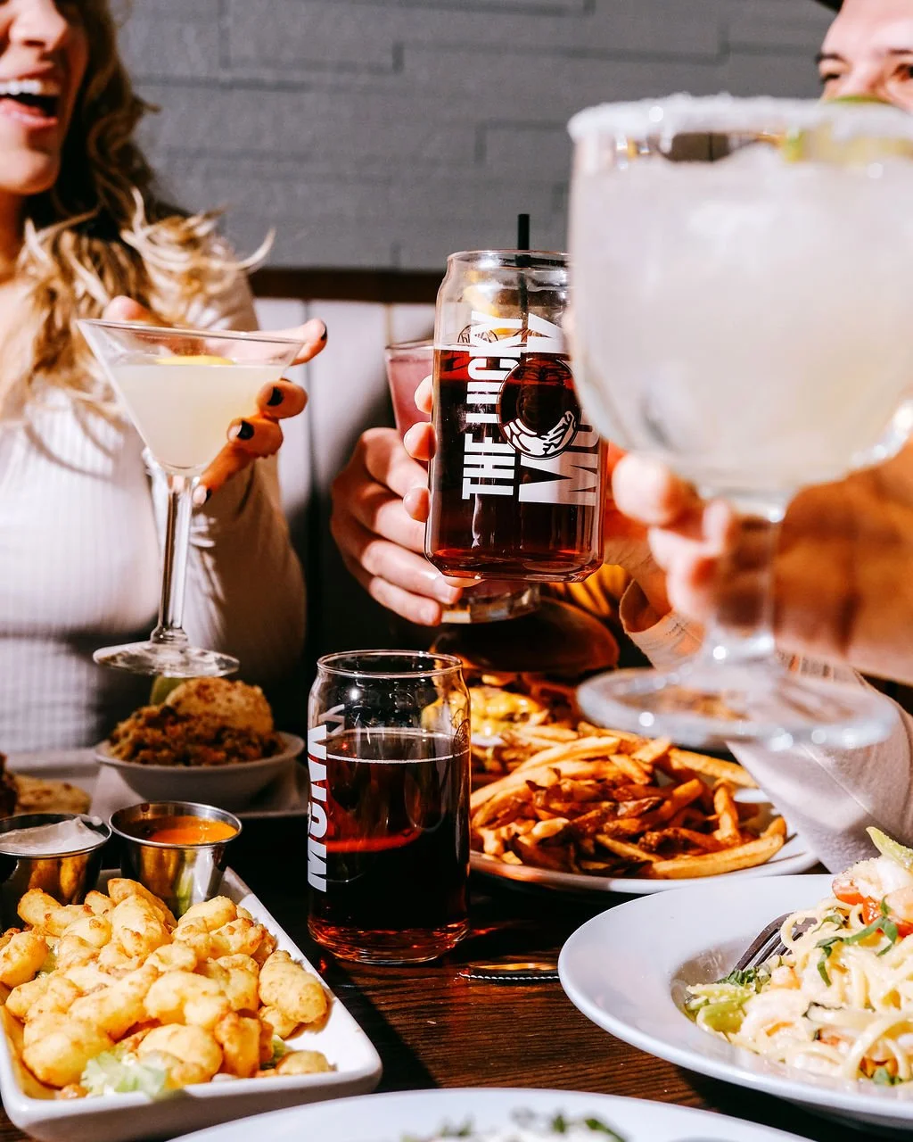 People enjoying drinks and food at a restaurant or bar, with cocktails, beer, and various dishes on the table.