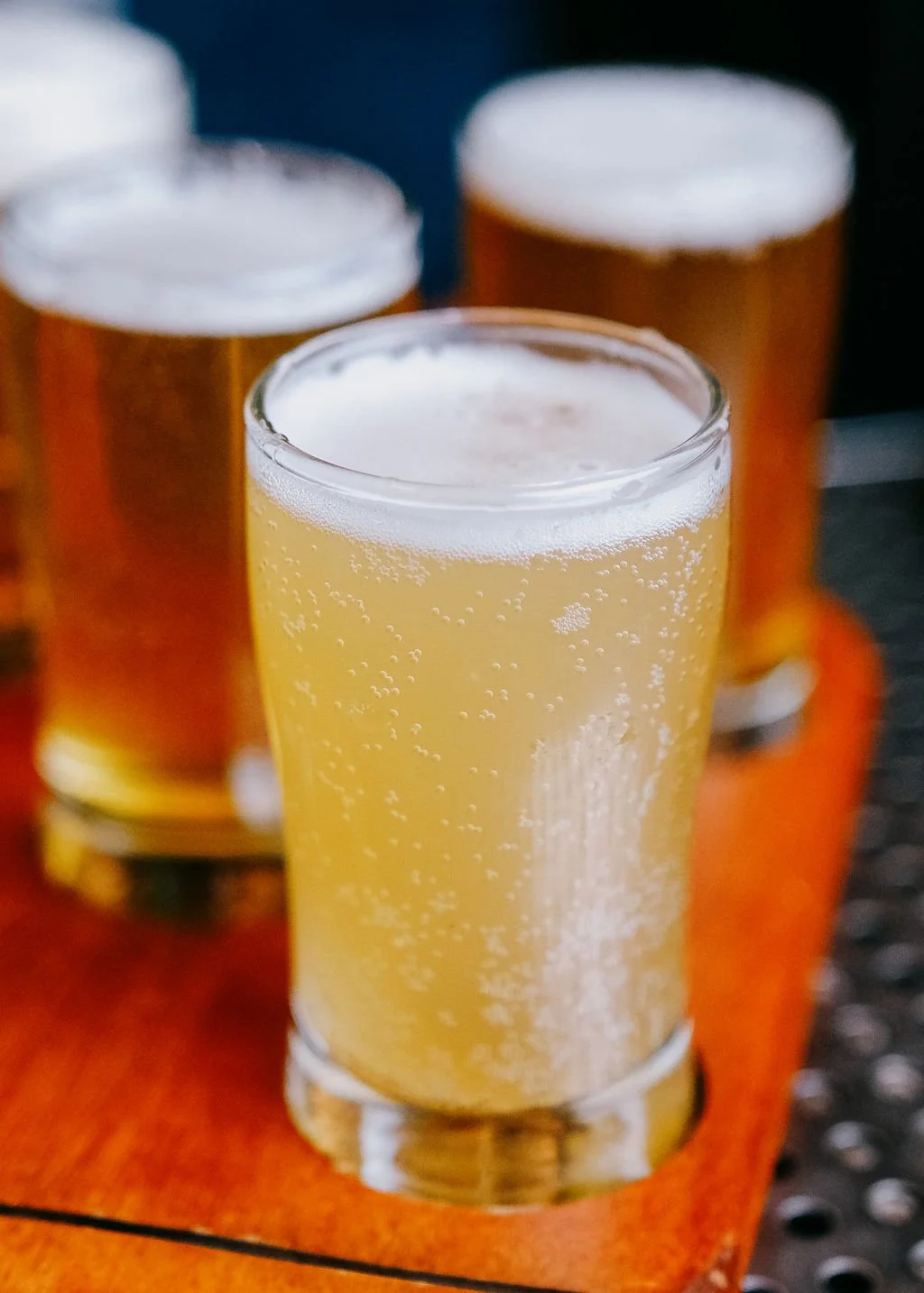 Close-up of a glass of light, fizzy beer with a foamy head, with three more glasses of beer in the background.
