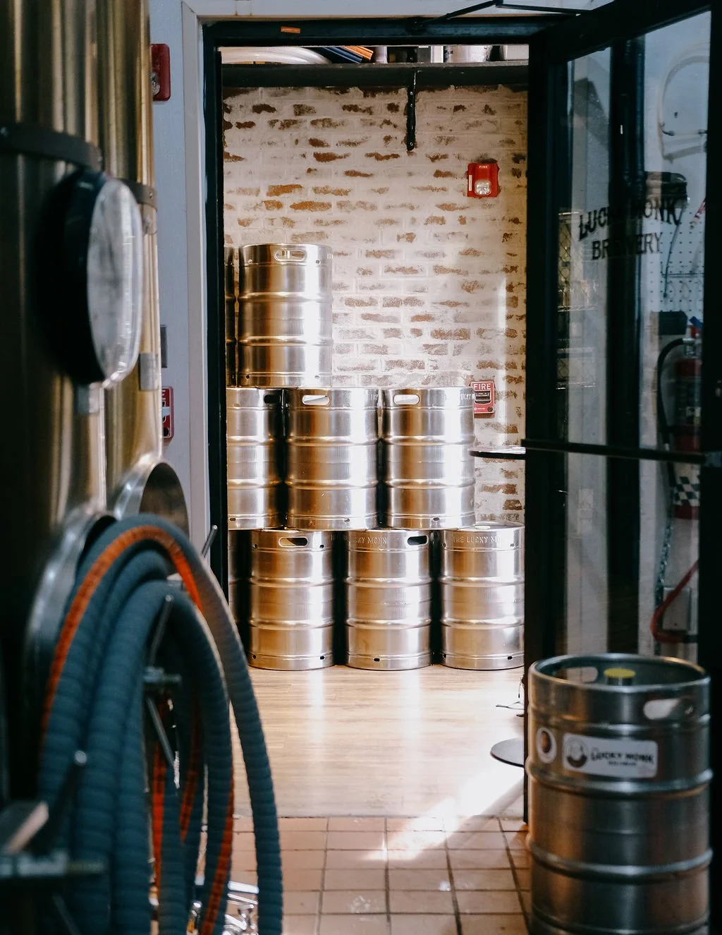 Stacked stainless steel beer kegs in a brewery storage room with exposed brick wall.