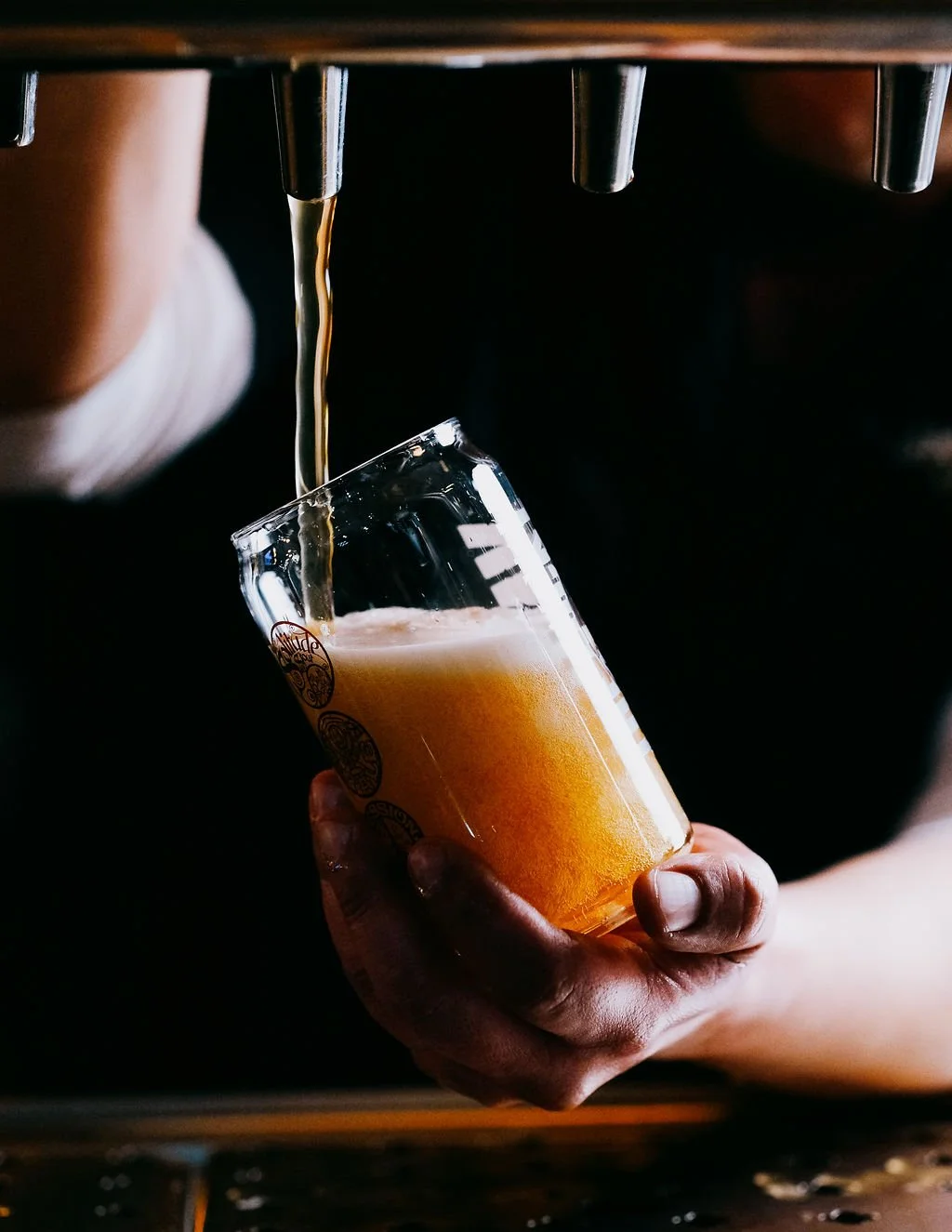 Pouring beer into a clear glass from a tap.