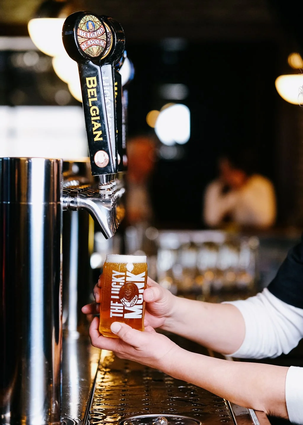 A person pours beer from a tap labeled 'Belgian' into a glass with the logo 'The New Molyk' at a bar.