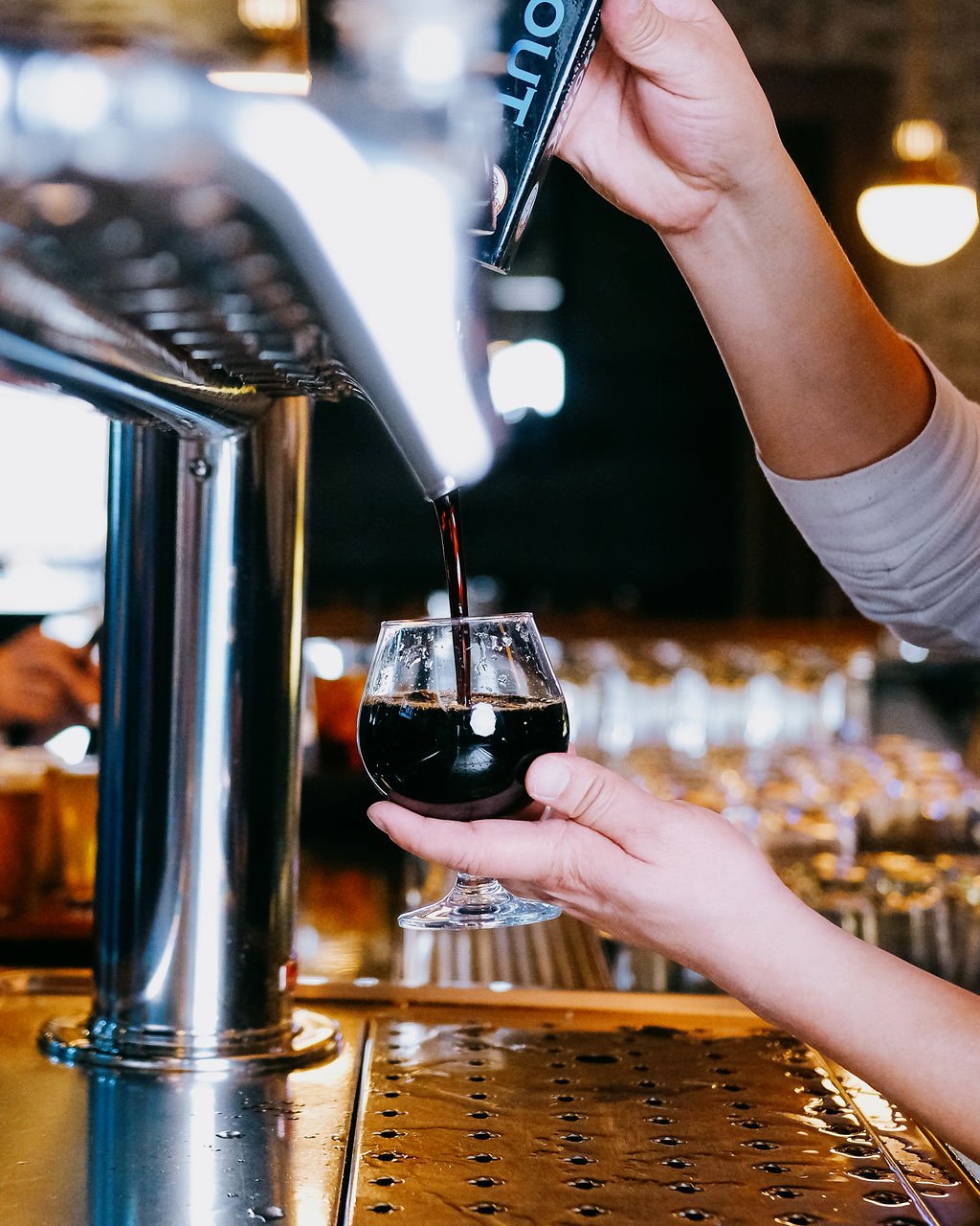 A person pours draft beer from a tap into a glass in a bar setting.