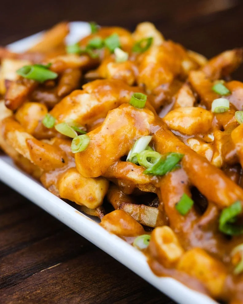Close-up of a white dish filled with chicken coated in orange sauce and garnished with chopped green onions.