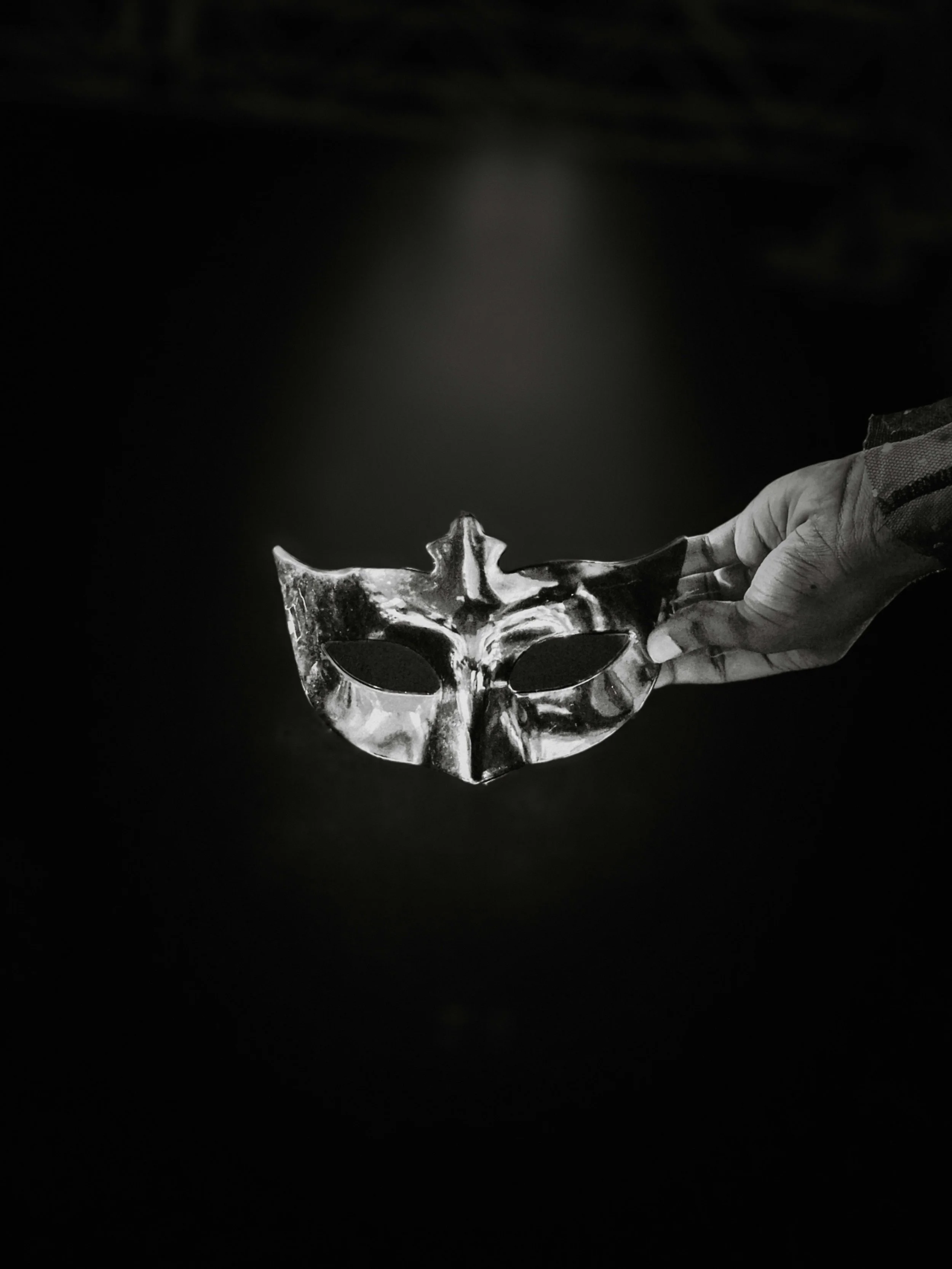 A hand holding a metallic mask resembling a skull on a dark background.
