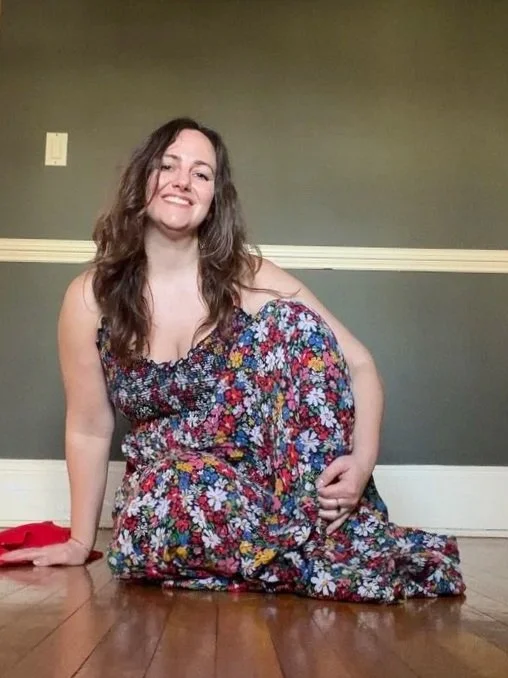 Woman in a colorful floral dress sitting on the floor with a smile.