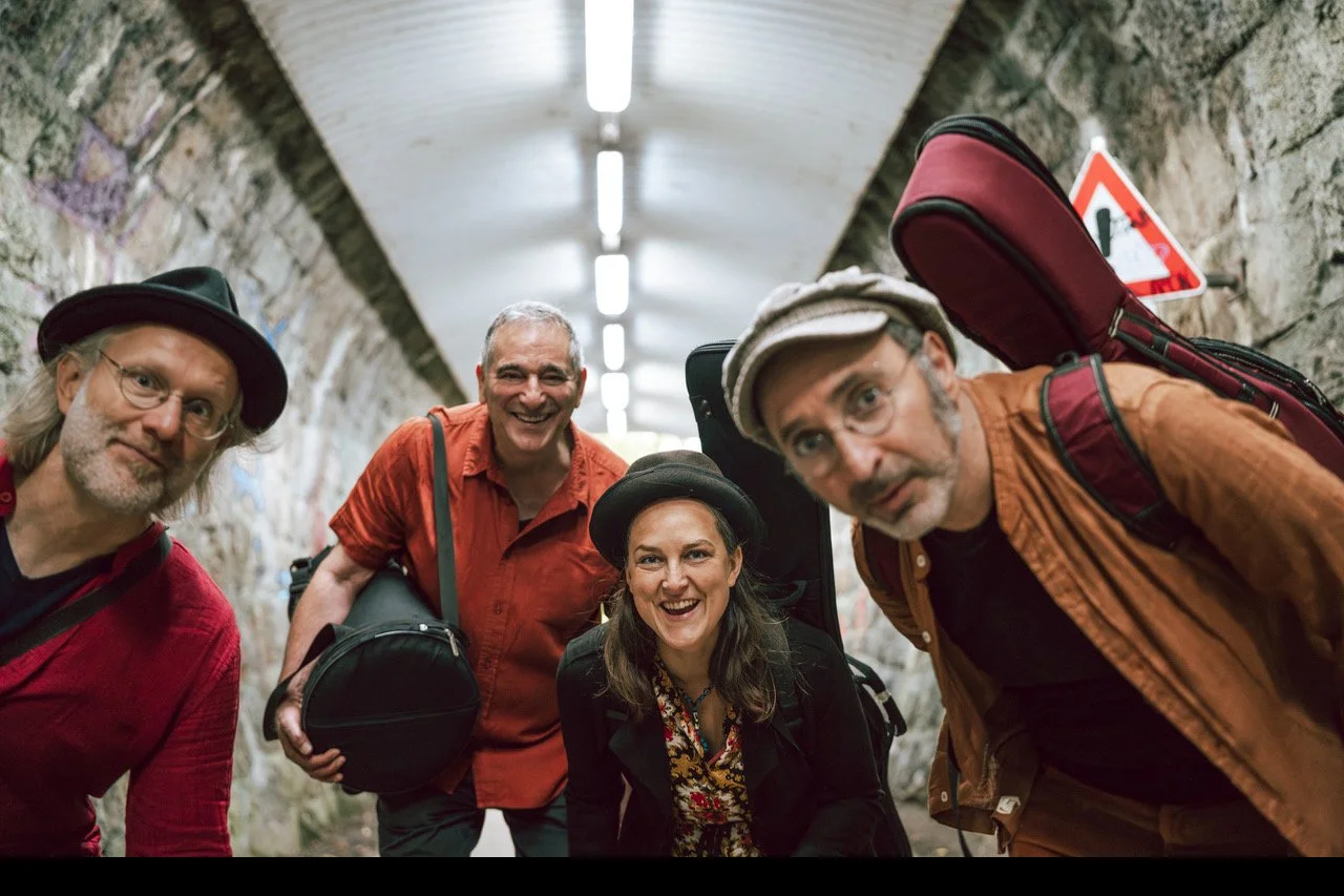 Fünf lachende Menschen mit Musikinstrumenten in einem Tunnel.