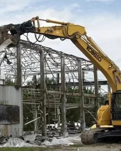 A large yellow Kobelco excavator demolishing a metal structure at a construction site.