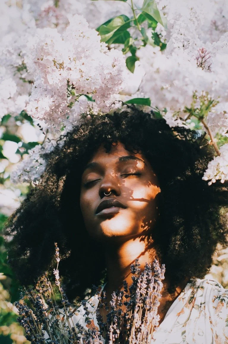 A black woman with an afro and nose ring stands under a hydrangea tree holding a bunch of lavender. Therapy for black women in codependent and enmeshed relationships