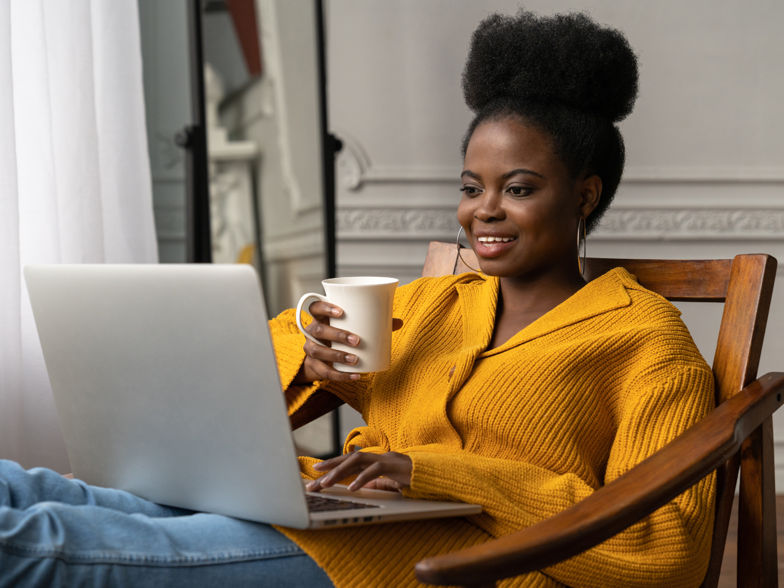 A Black Woman in a yellow sweater sits with a cup of coffee and a laptop on her lap. Virtual Therapy for Queer Black Women in Los Angles