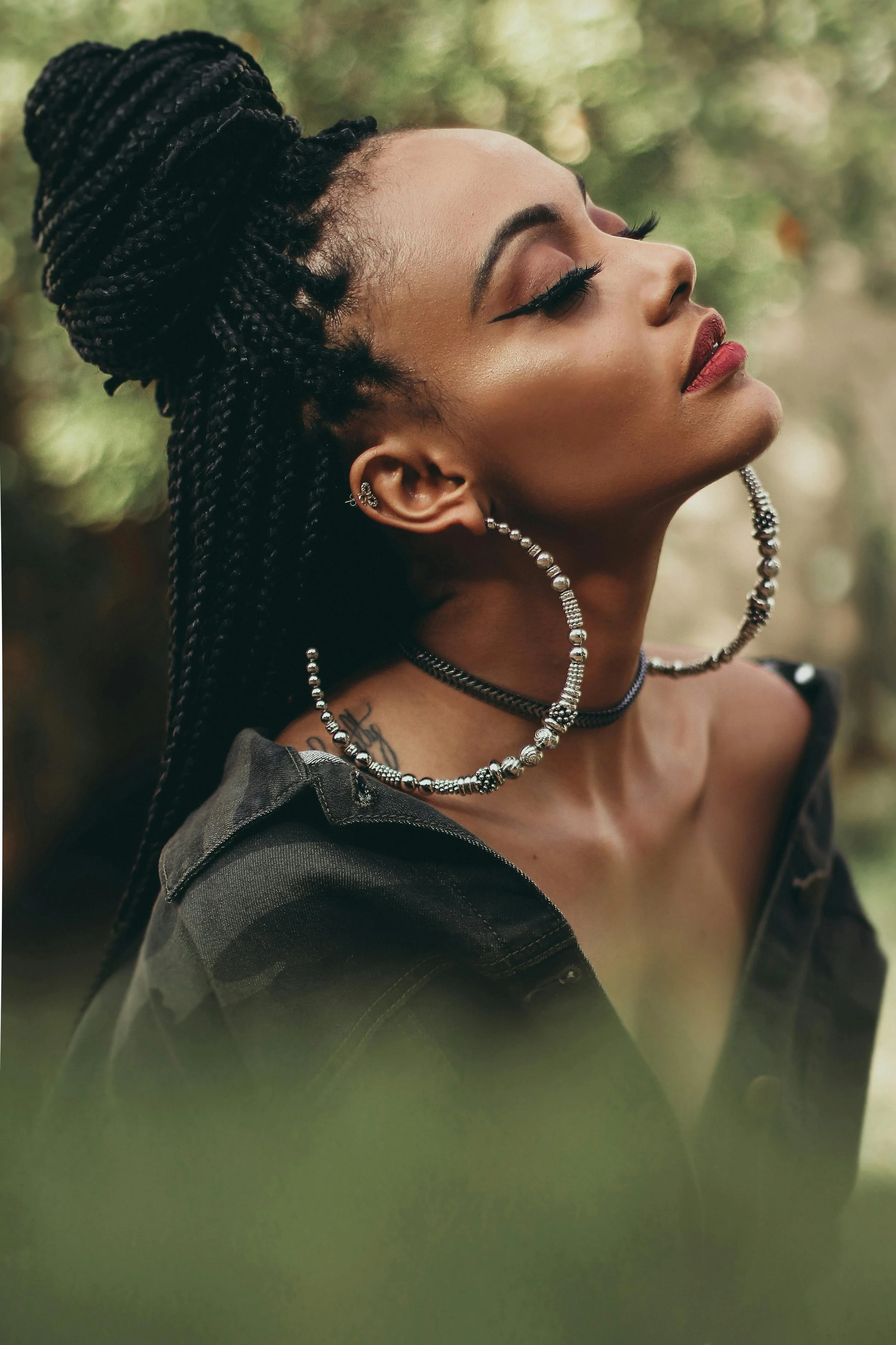 A black woman with box braids and gold hoop earrings looks up with her eyes closed. Therapy for black women embracing embracing their true selves.