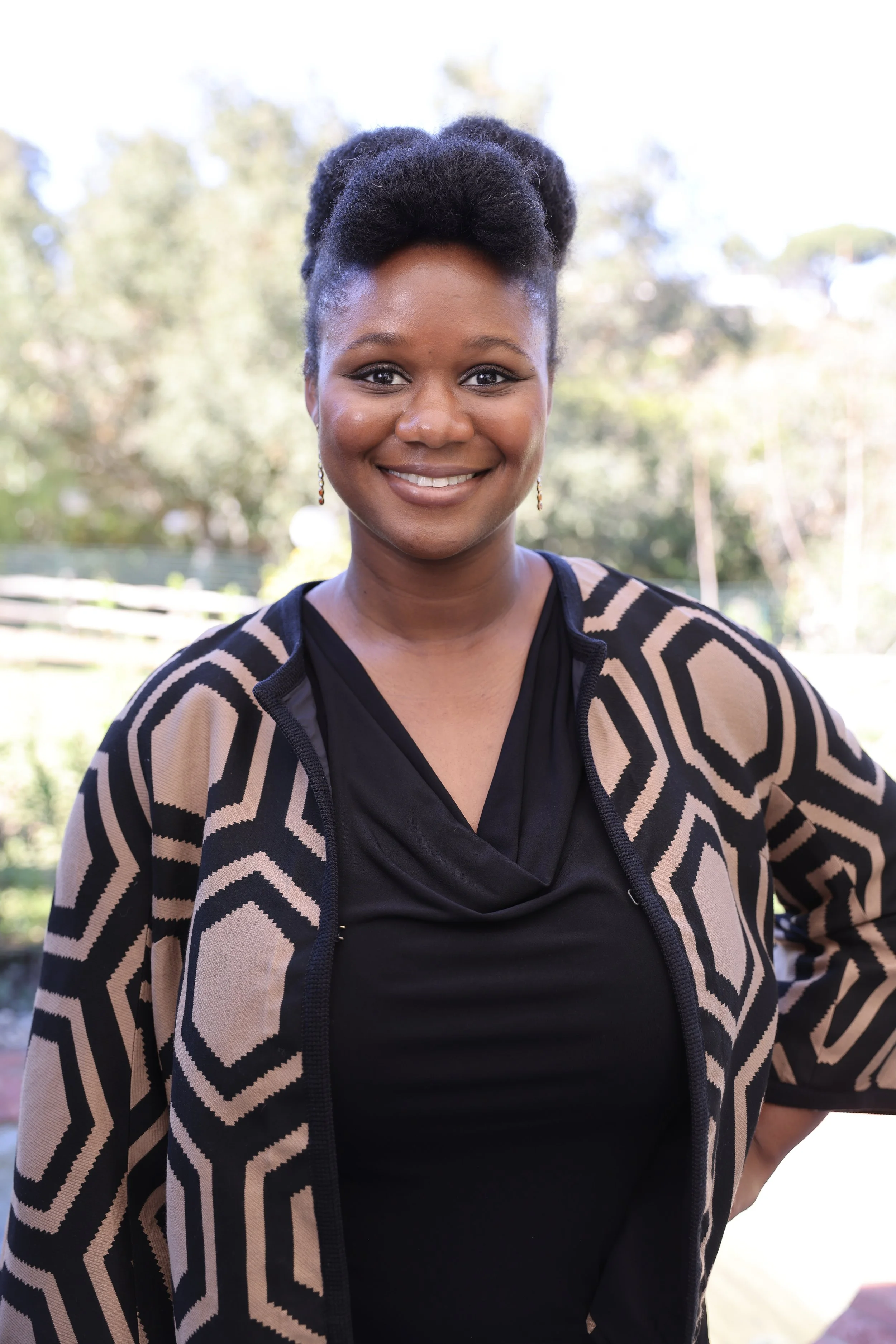 Crystal Clark a Black Female Therapist in Los Angeles stand smiling in a black shirt and brown and black cardigan.