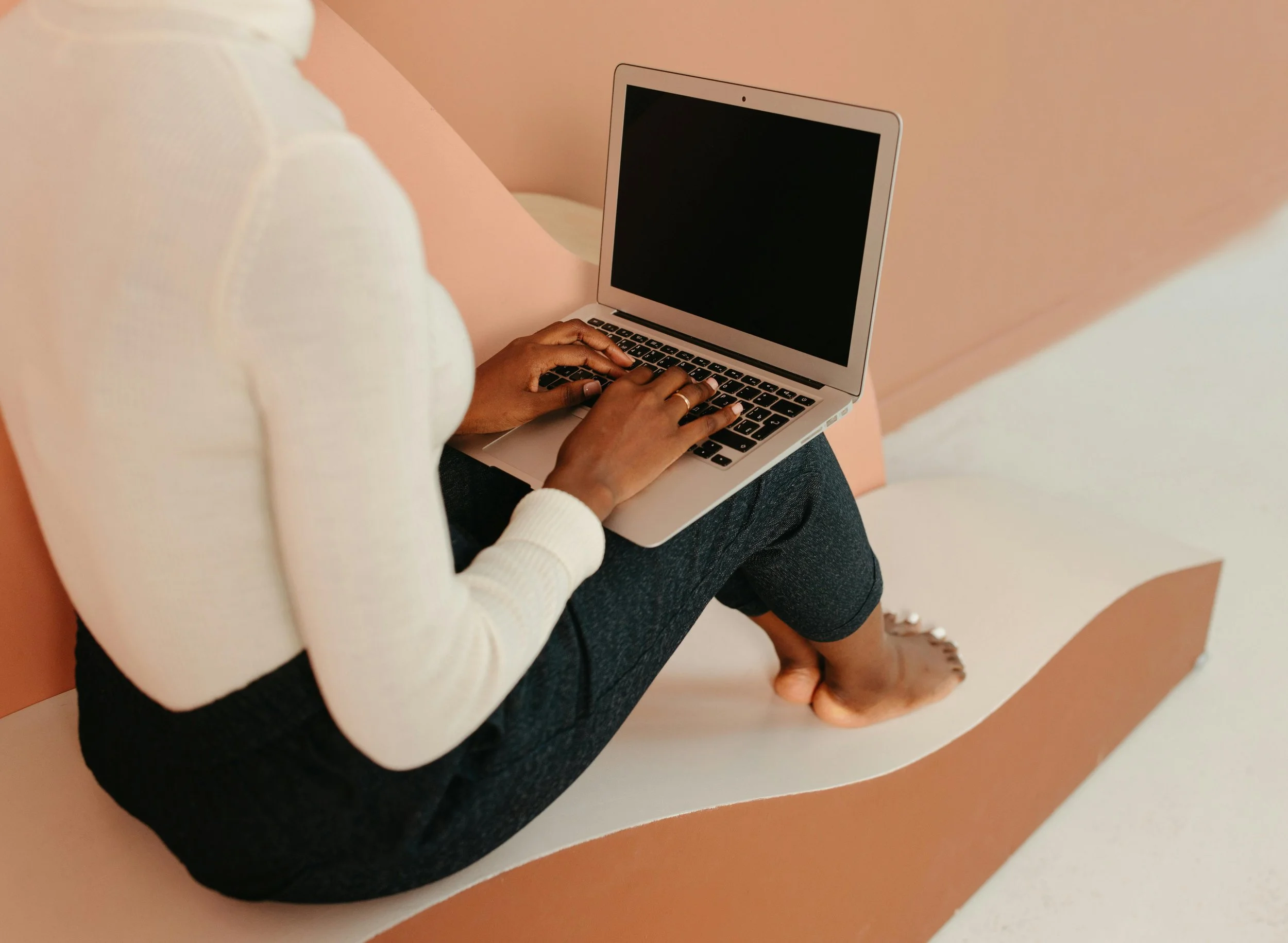 A black woman has a laptop perched on her knees. Virtual therapy for BIPOC women in Los Angeles